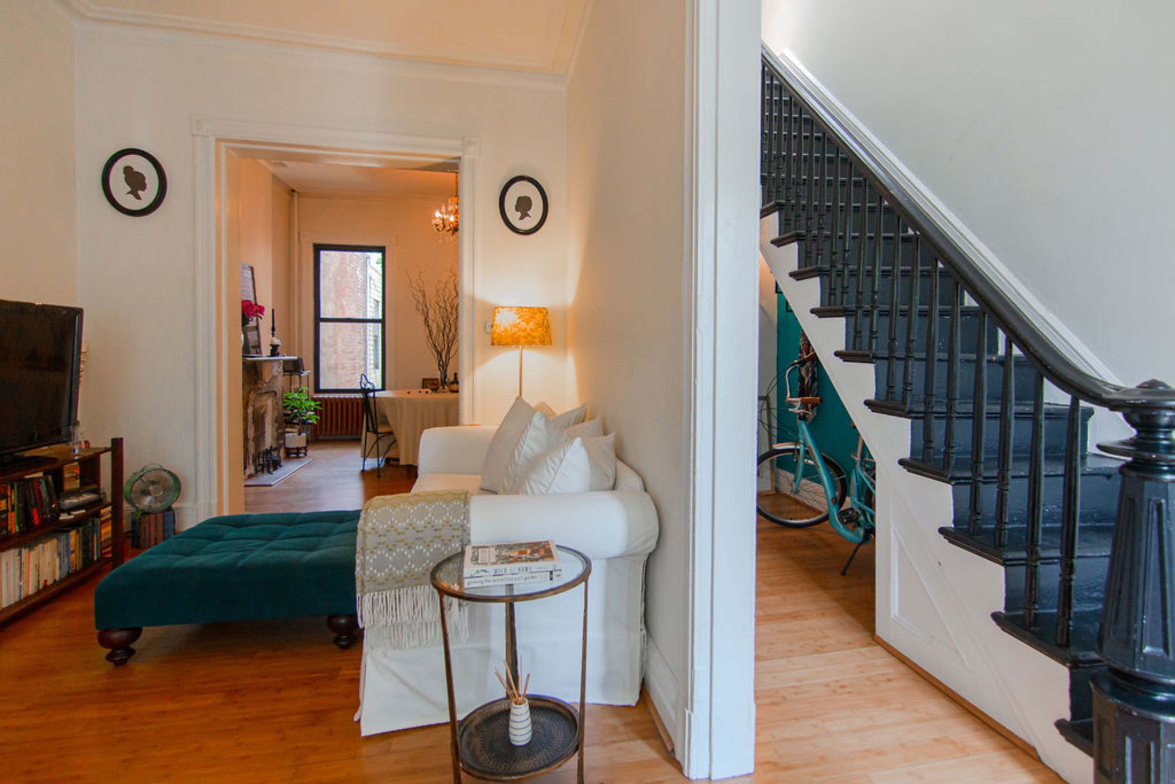 A cozy living area featuring a white sofa with a teal ottoman, a small side table, and a glimpse of a staircase leading to a second floor.