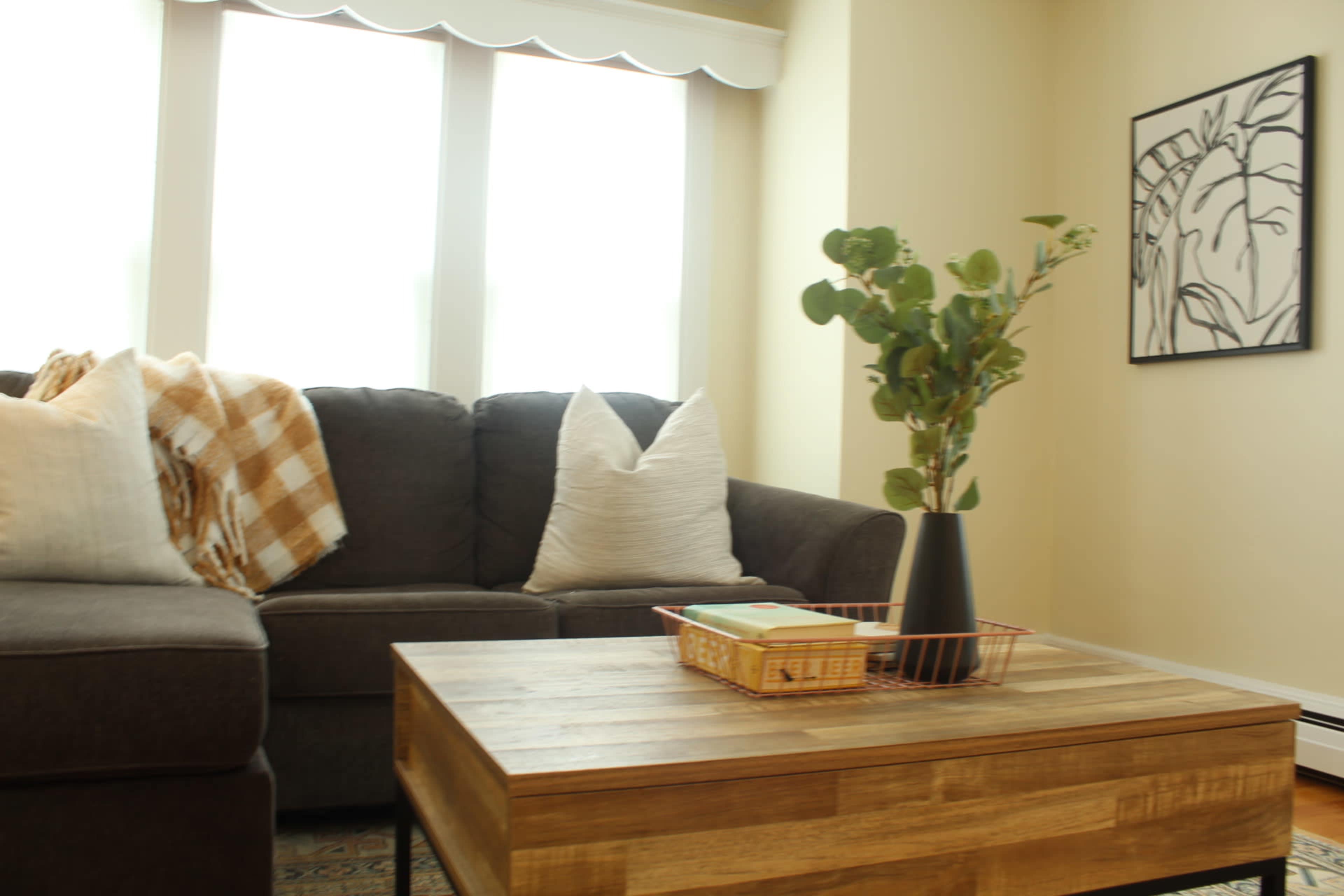 A cozy living room with a dark gray sectional sofa, a wooden coffee table, and a decorative vase with greenery on the table.