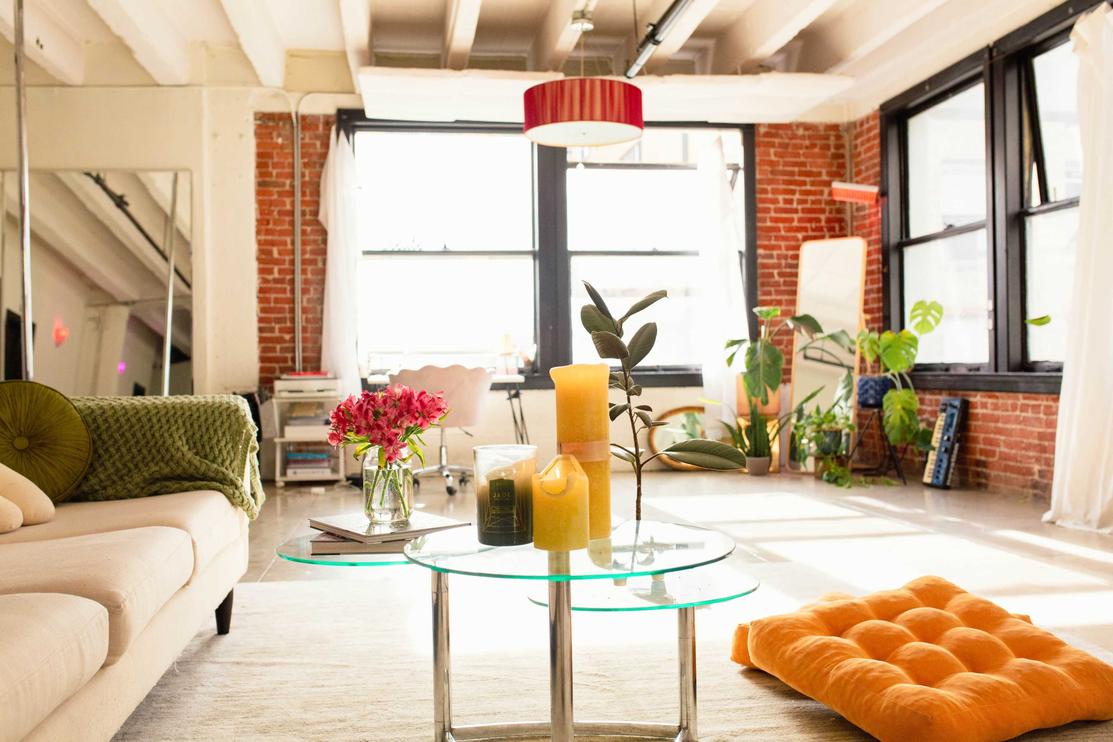 A bright, modern apartment with a cozy seating area, a glass coffee table adorned with candles and flowers, and large windows allowing natural light to fill the space.