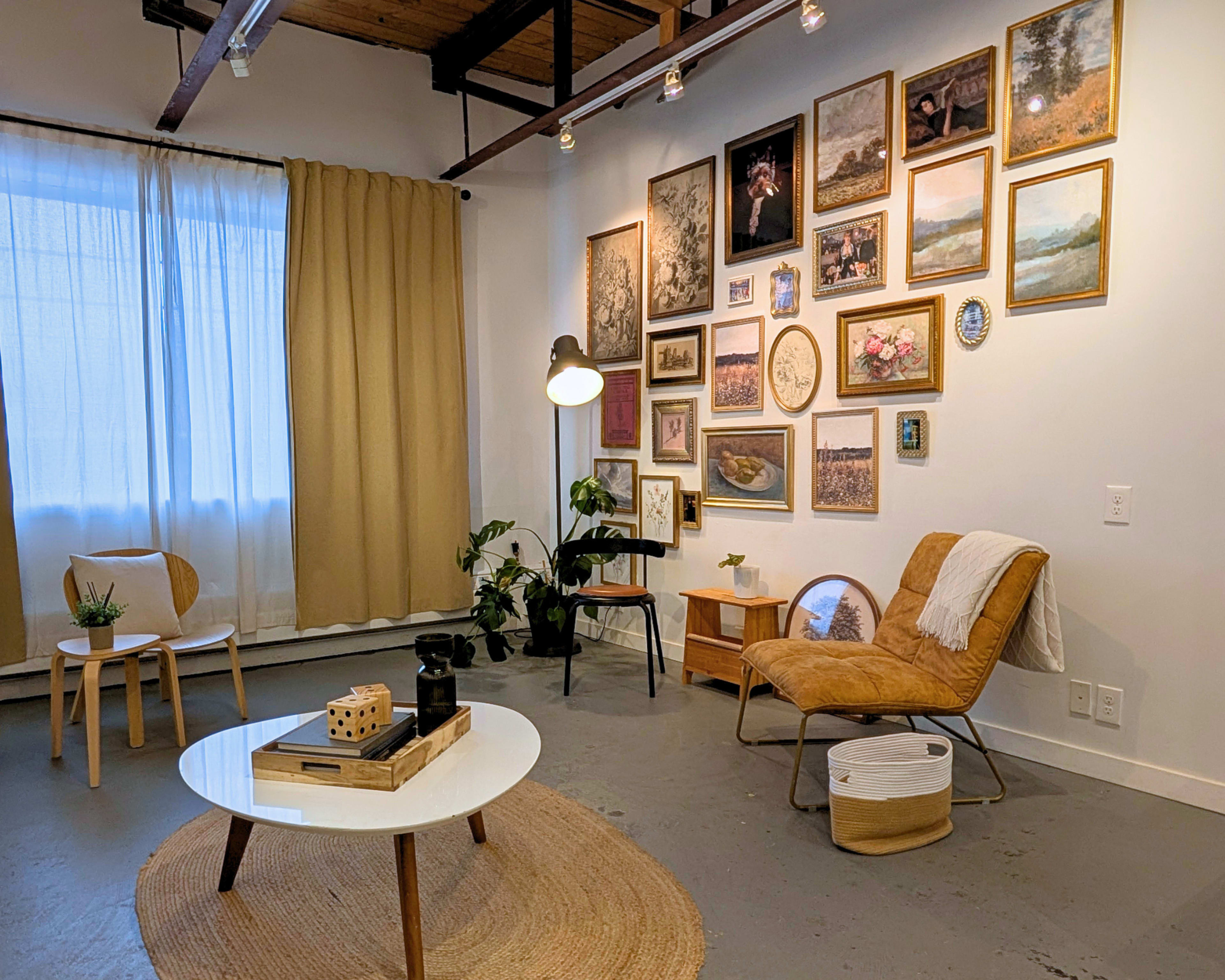 The image shows a cozy room with a seating area featuring a chair, a table, and a gallery wall adorned with various framed artworks.