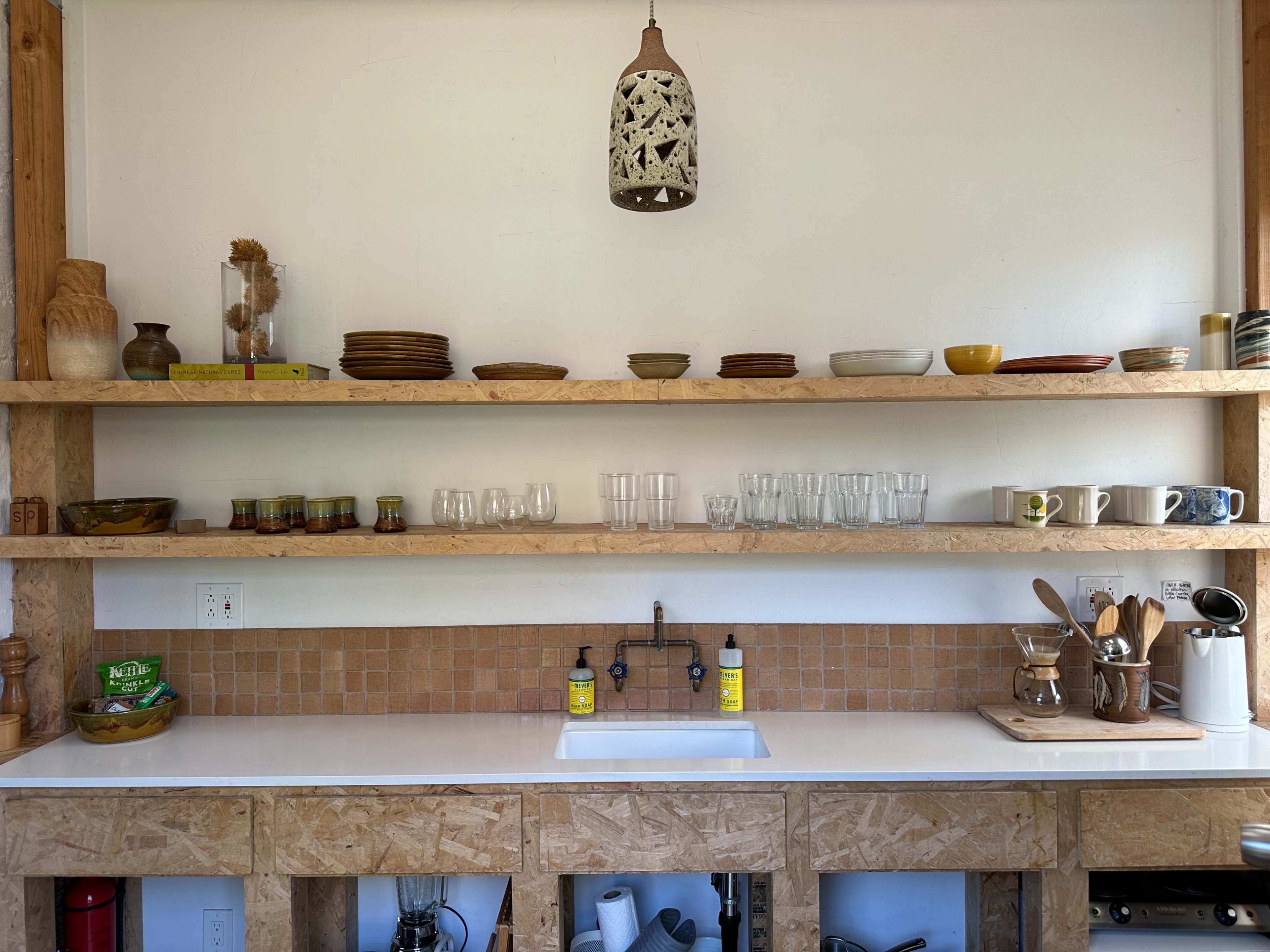 A tidy kitchen shelf holds various dishes and glassware above a white countertop and sink.