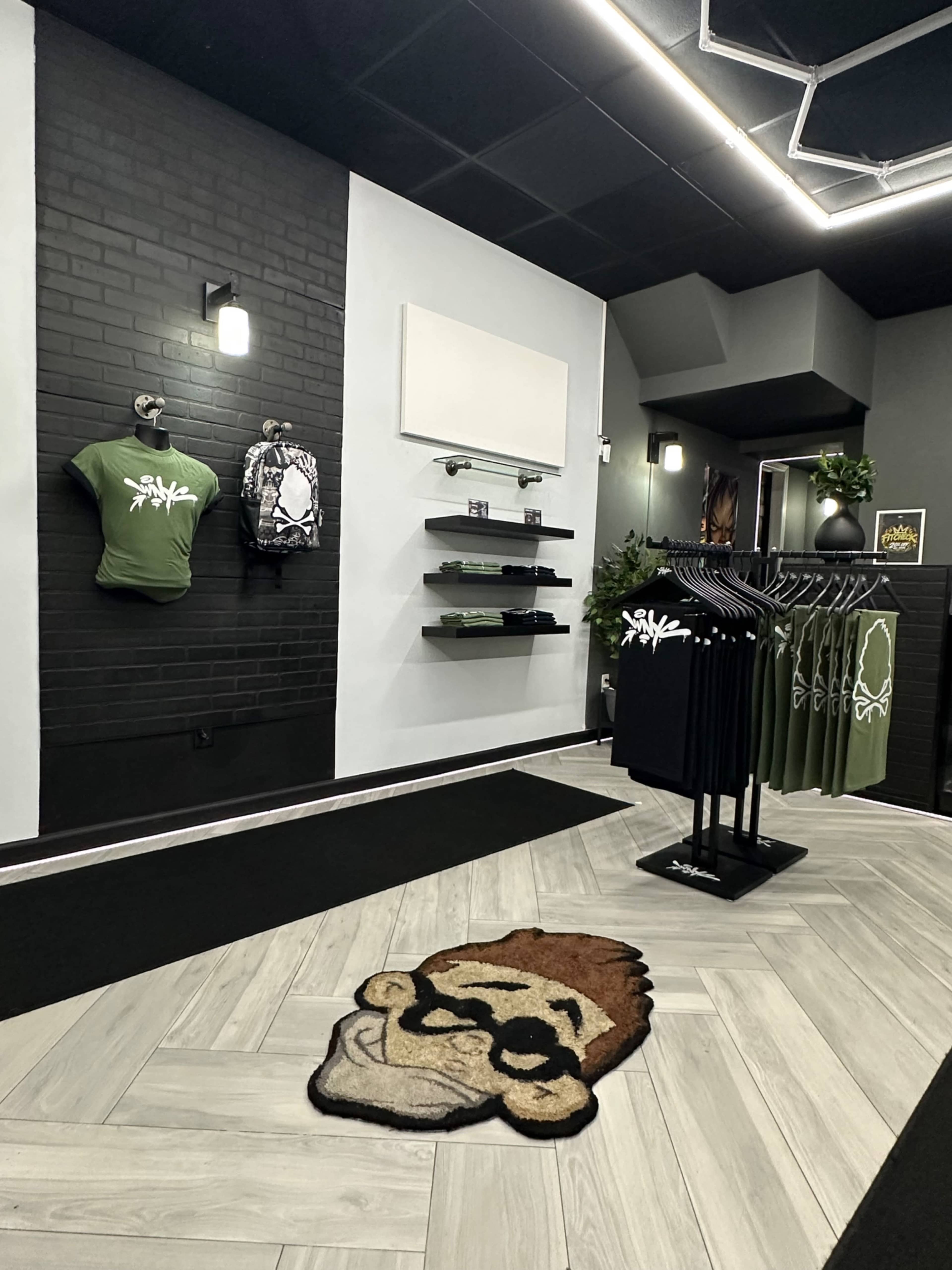 The image shows a retail store interior featuring clothing displays, including green shirts and black clothing hanging on racks, as well as a cartoon-themed rug on the floor.