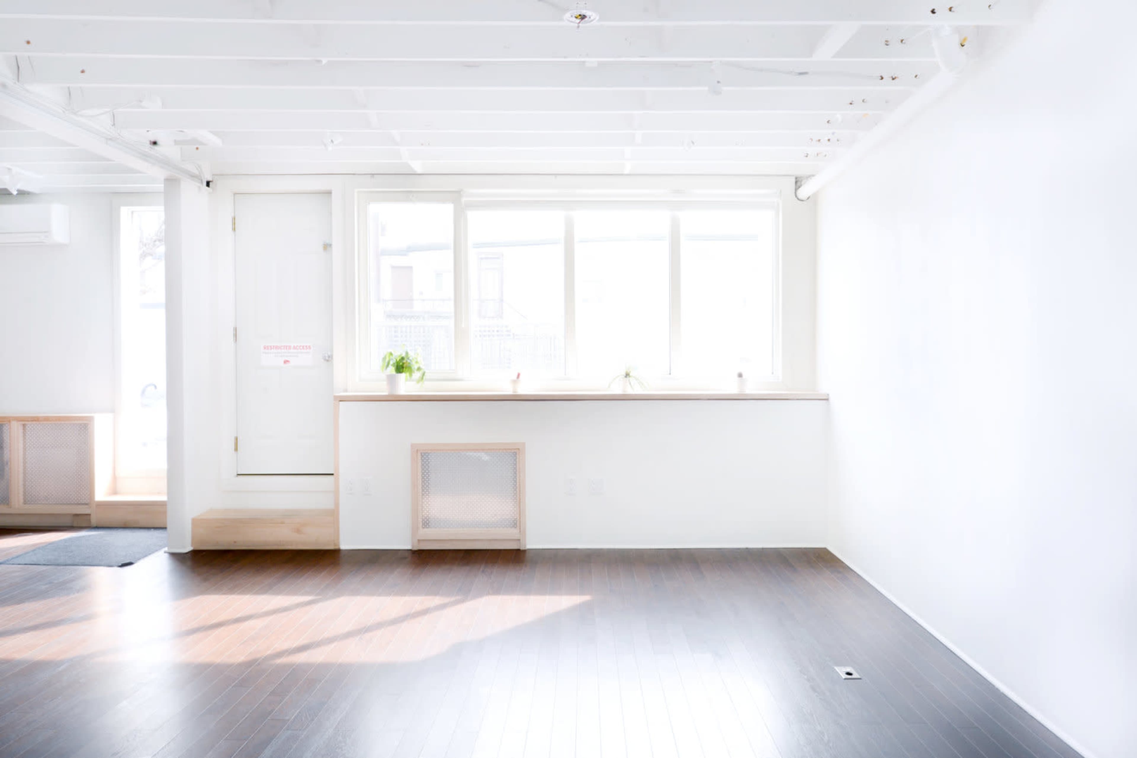 A bright, minimalist room with white walls, wooden flooring, and a large window above a simple countertop.