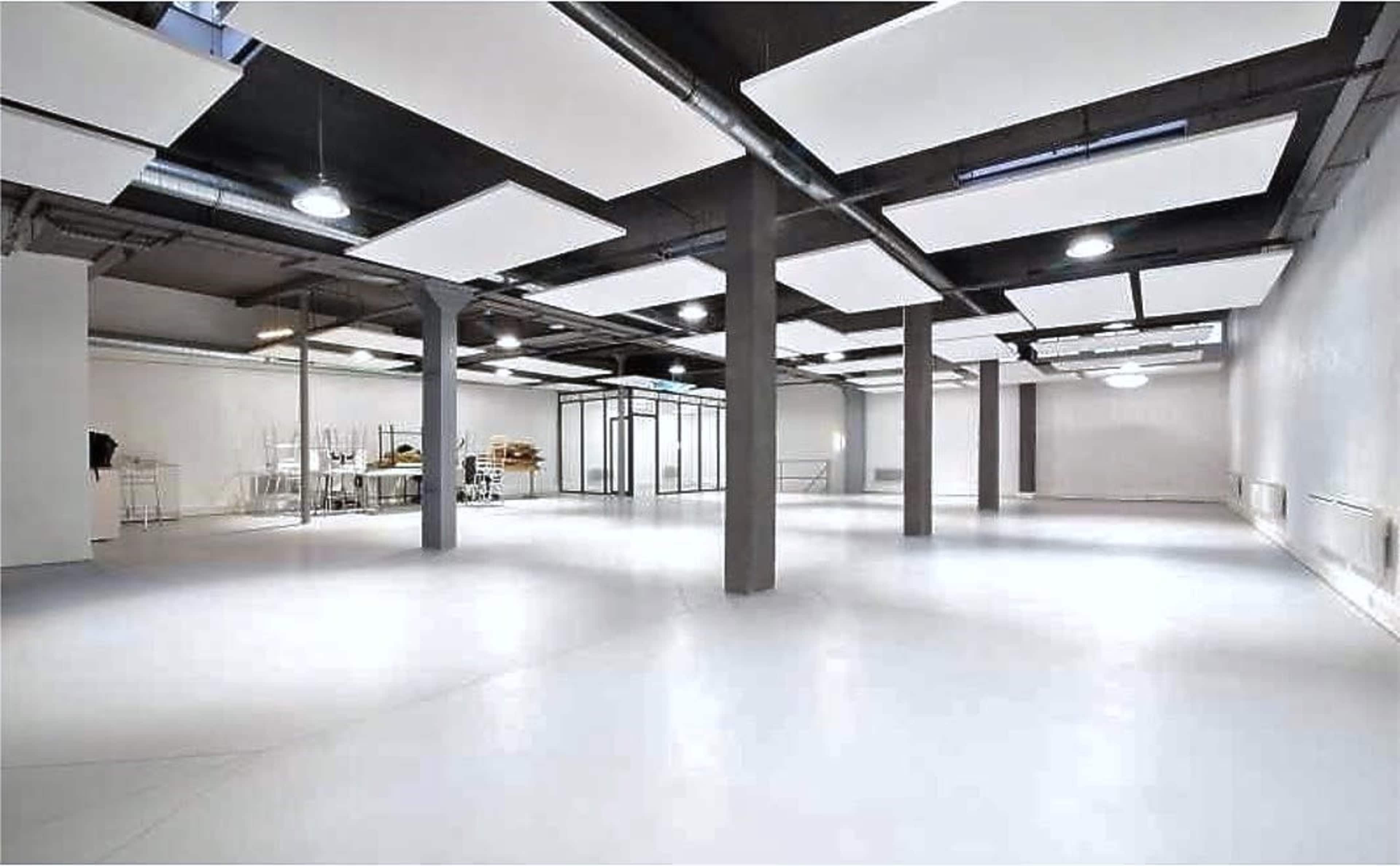 A spacious, empty room with white walls, a polished floor, and several hanging ceiling panels.