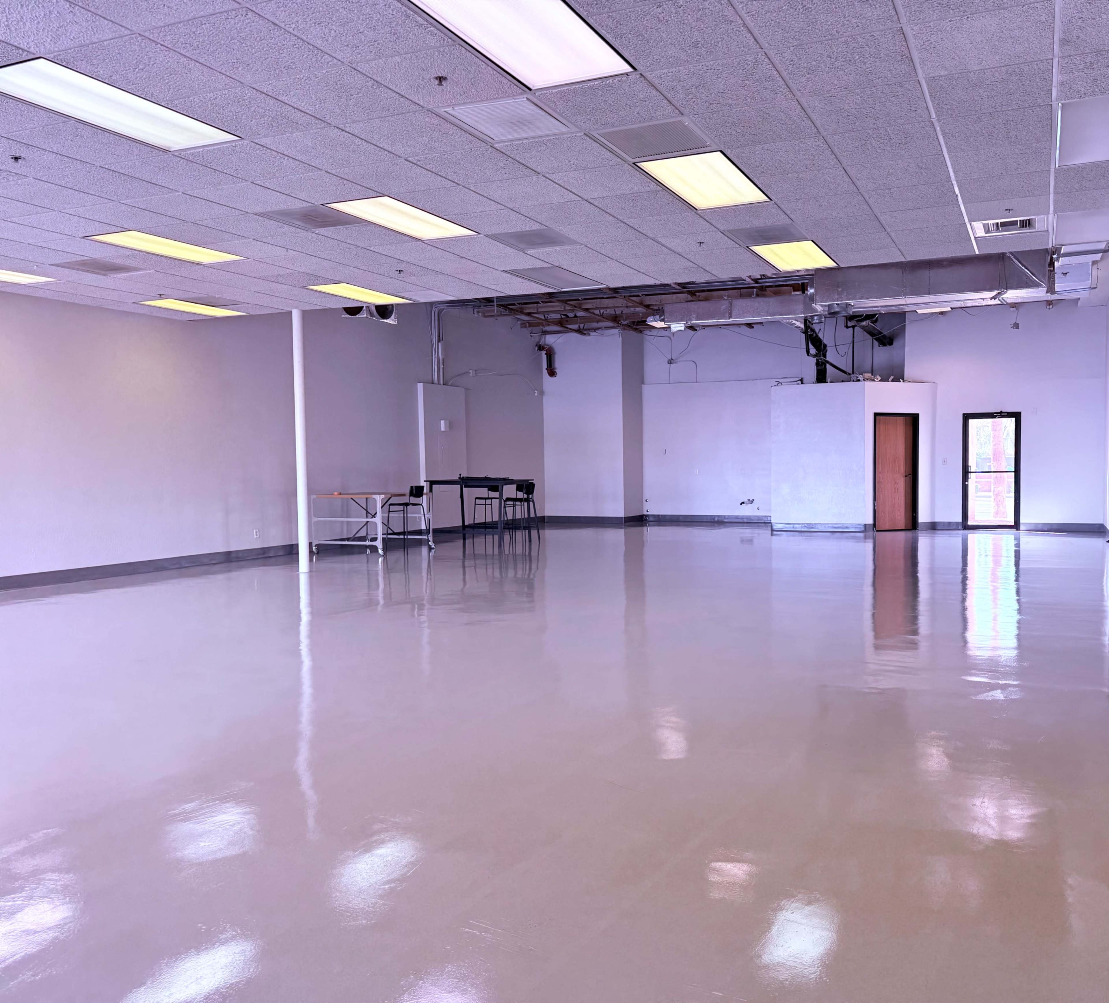 The image shows a spacious, empty room with polished floors, overhead fluorescent lights, and minimal furnishings.