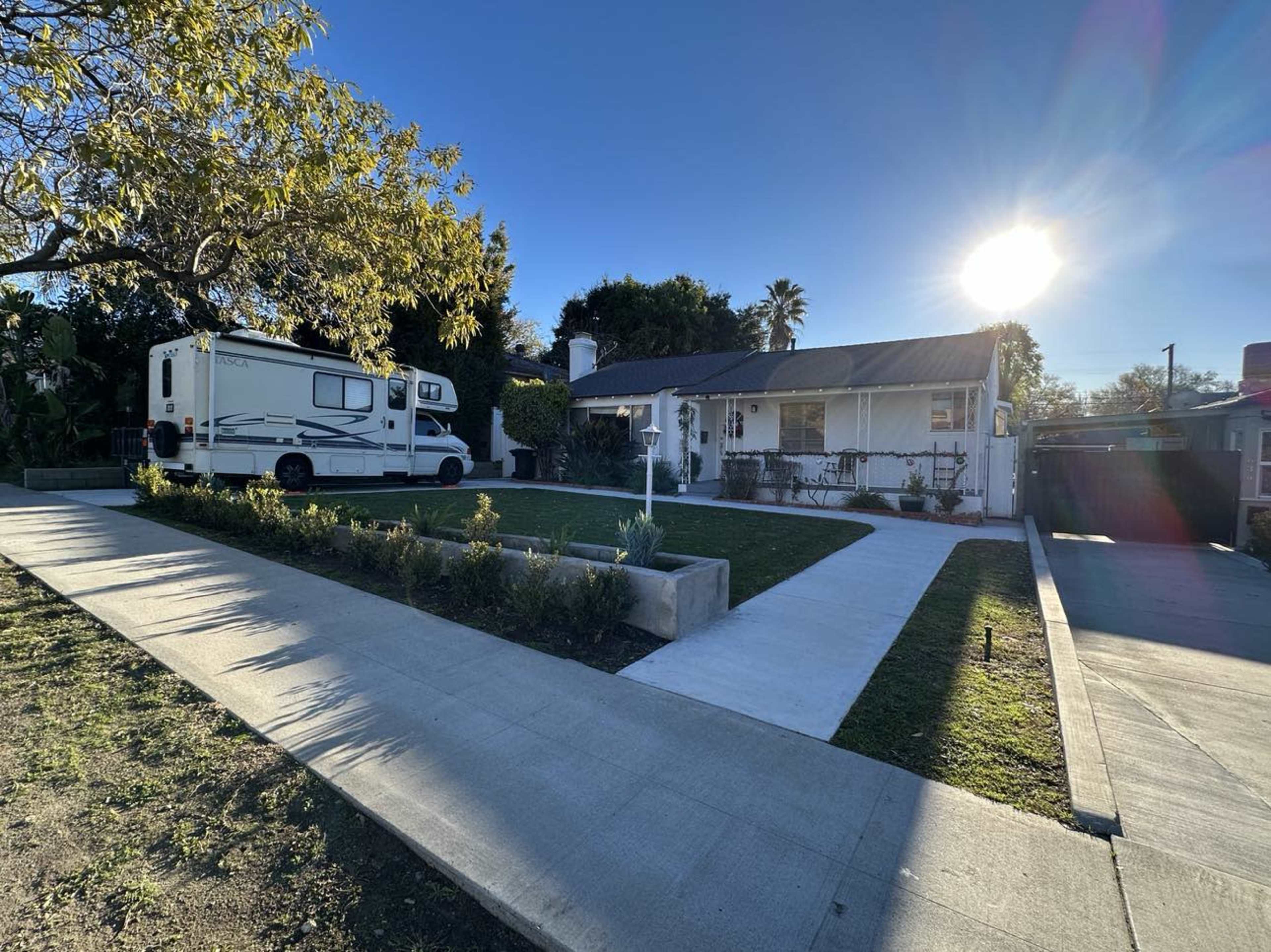 A recreational vehicle is parked in front of a single-story house with a landscaped yard and a clear blue sky overhead.