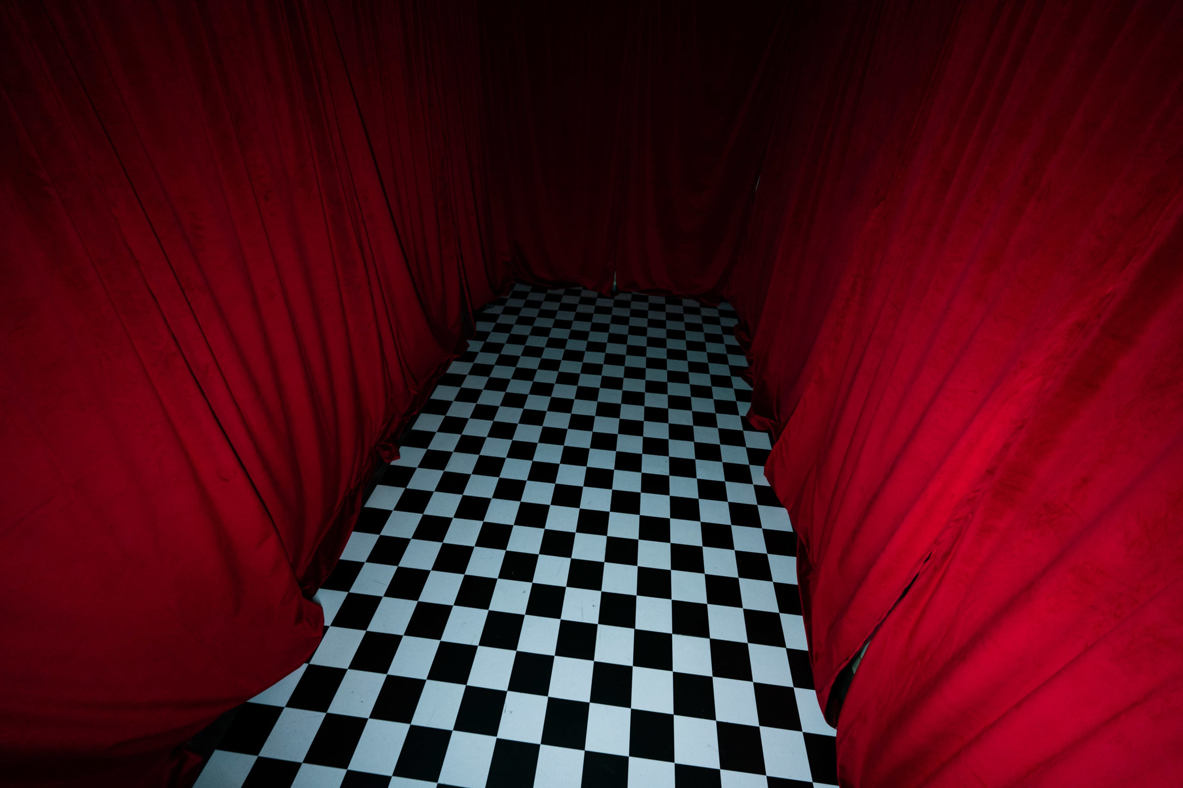 A checkered black and white floor is framed by red curtains in a dimly lit space.
