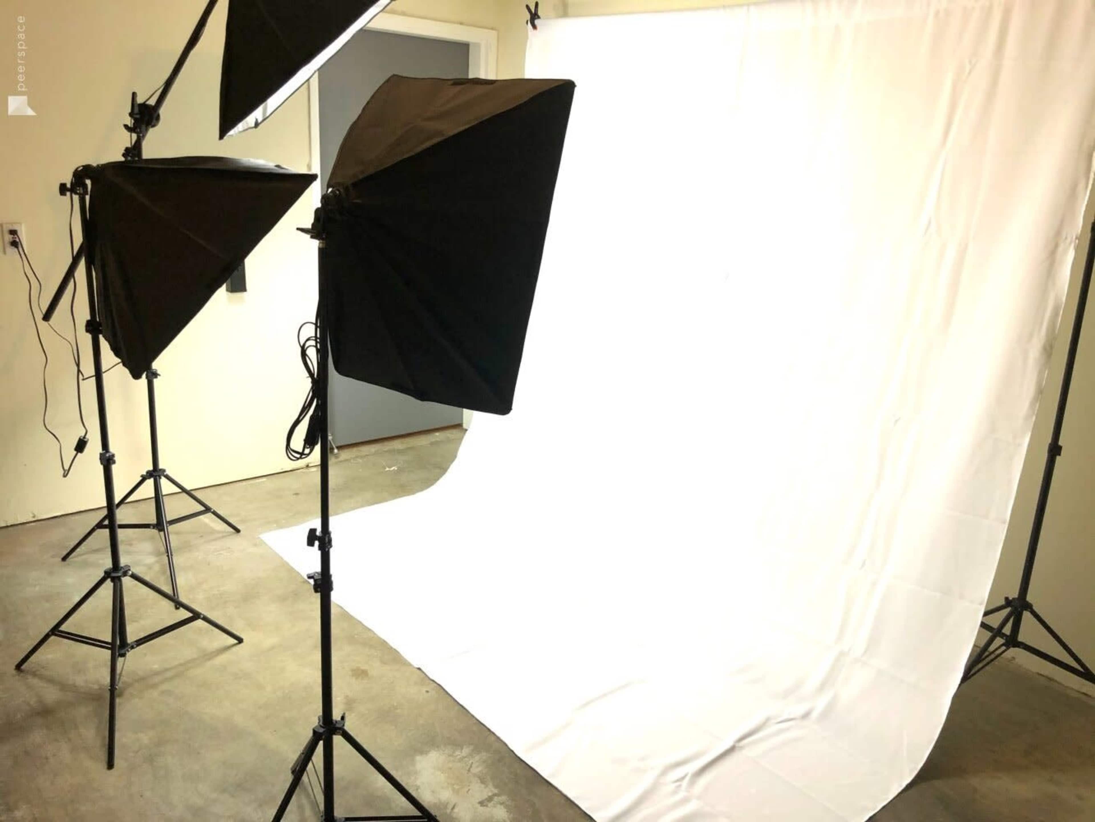 A photography studio setup with three softbox lights directed towards a plain white backdrop.
