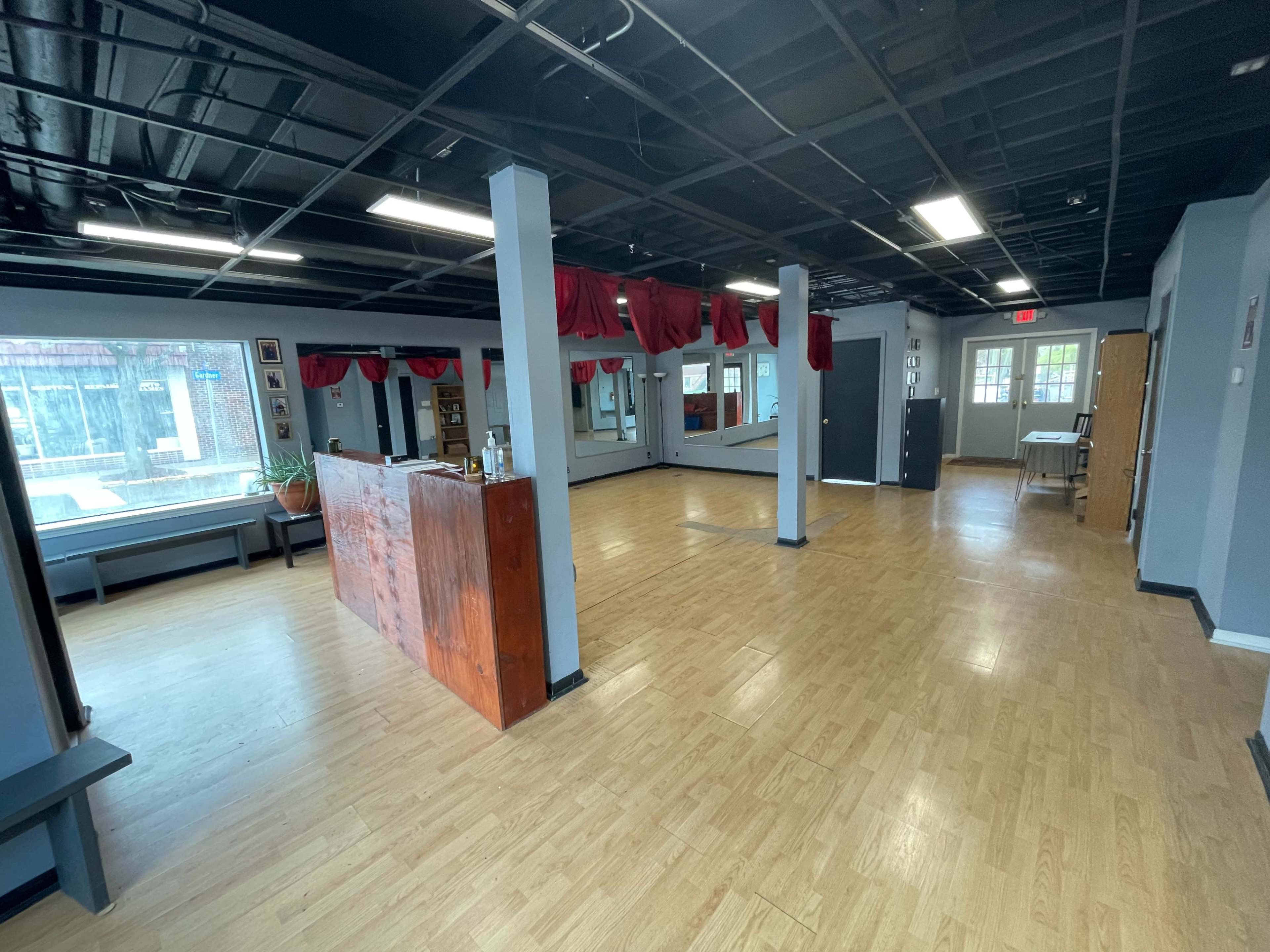 An empty dance studio featuring wooden floors, several mirrors, and a reception area with a wooden counter.