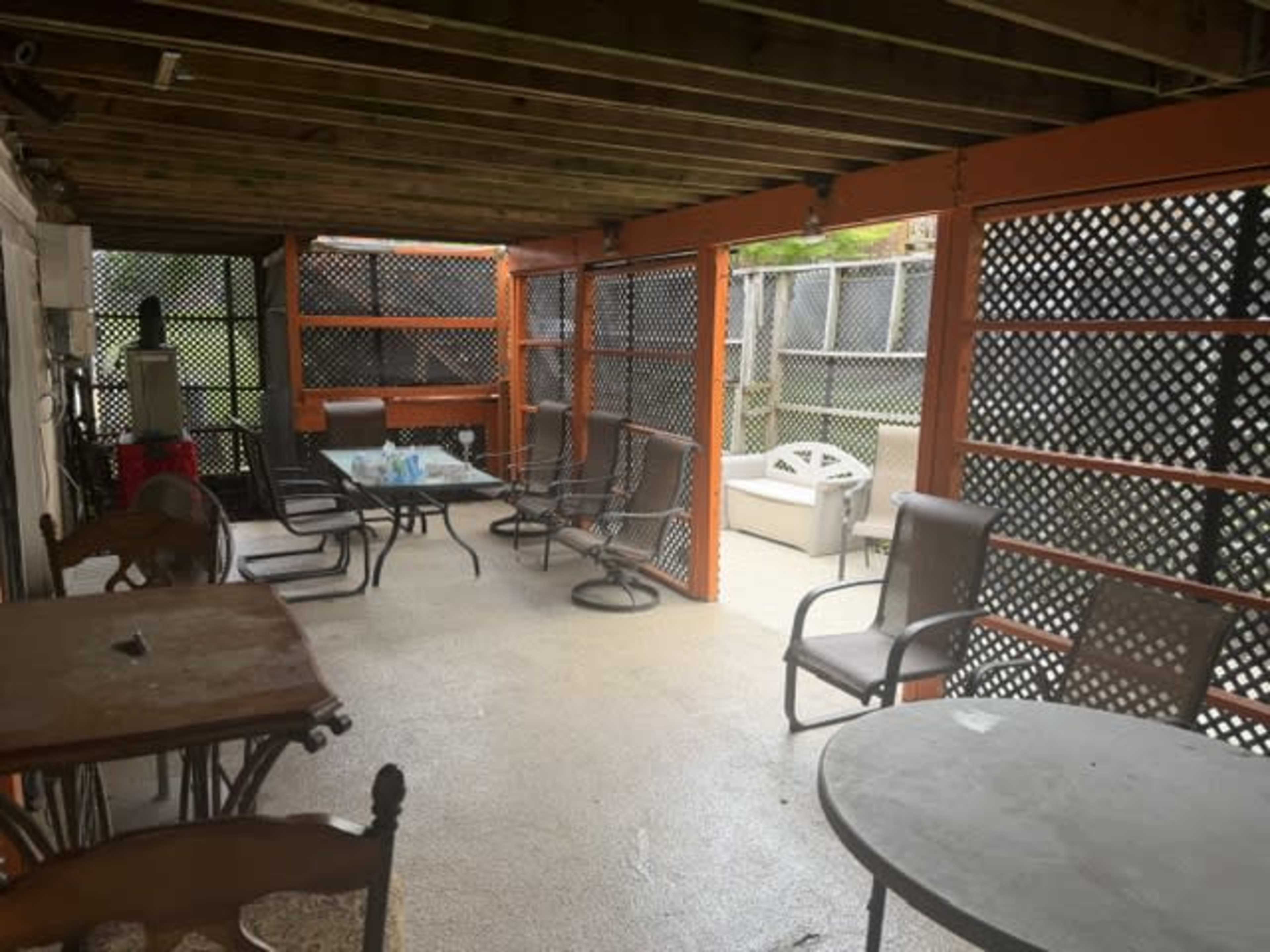The image shows a covered outdoor patio with several tables and chairs arranged inside a lattice fence structure.