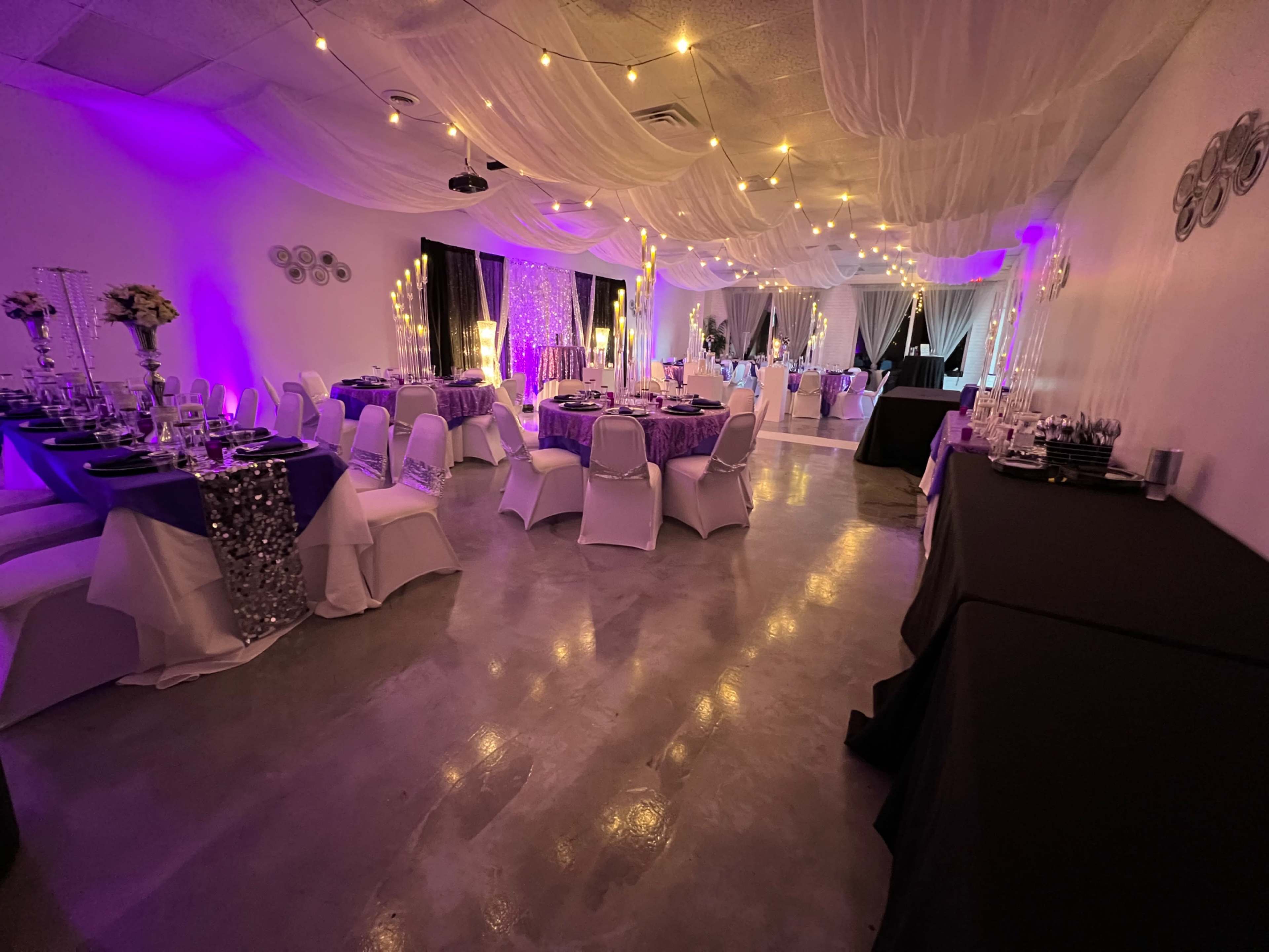 An event space with elegantly set tables, draped fabric, and string lights creating a festive atmosphere.