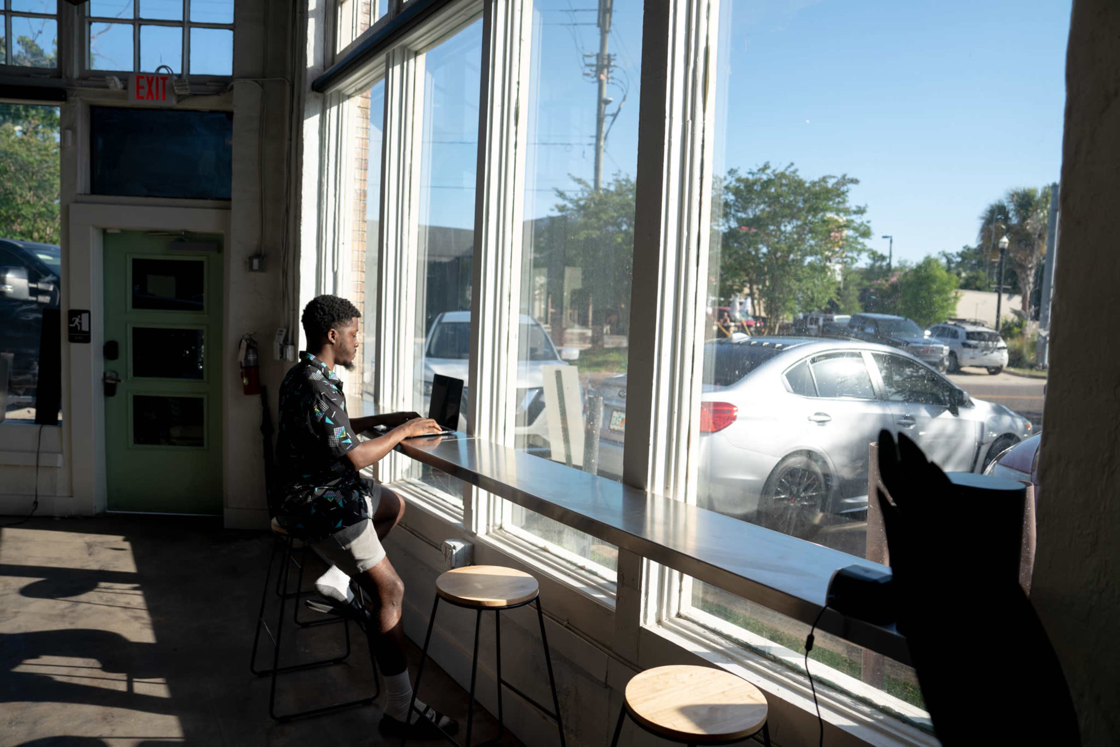 A person sits at a window-side counter using a laptop in a bright, sunlit café.