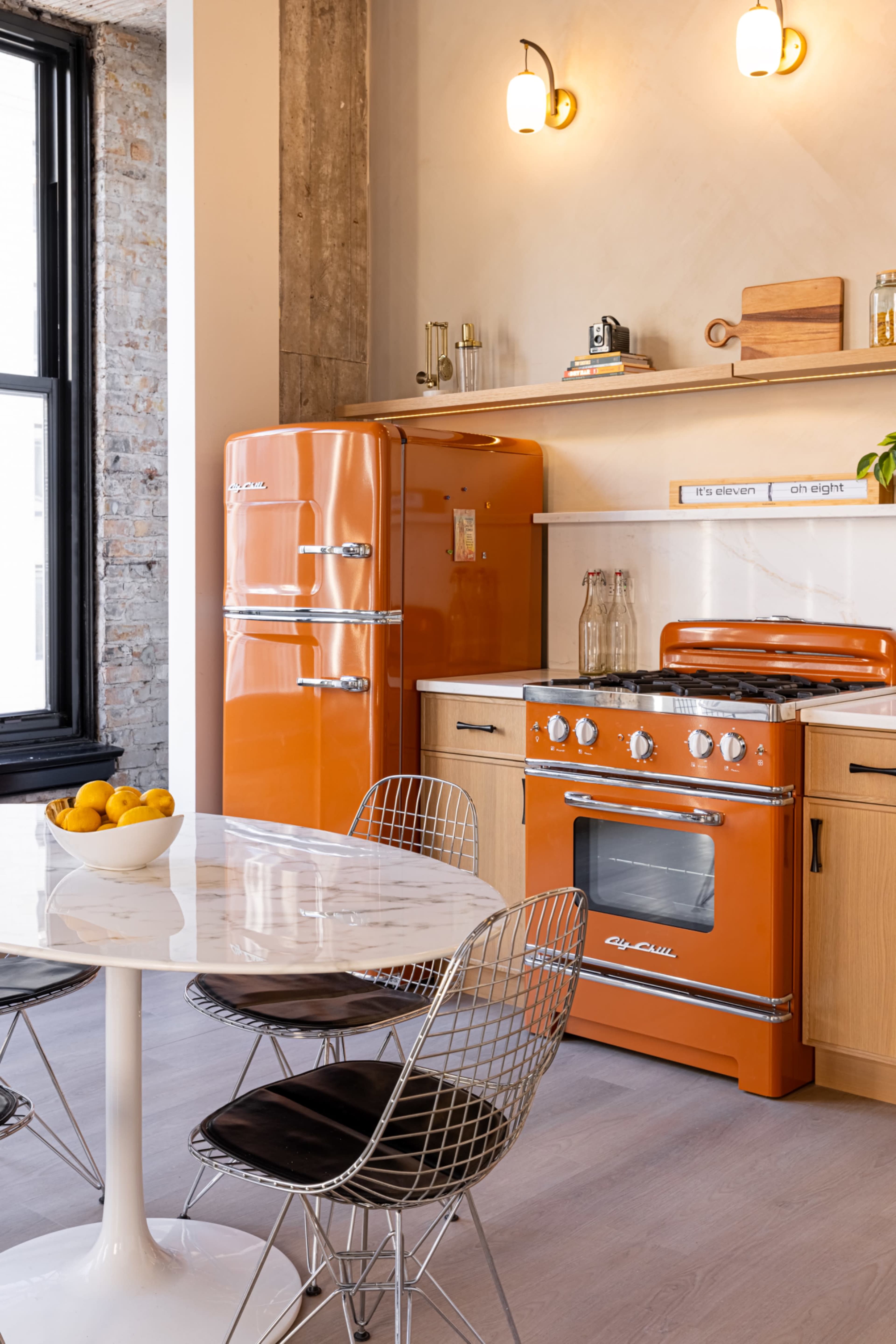 The kitchen features orange retro appliances, a marble-topped dining table, and modern wire-frame chairs.