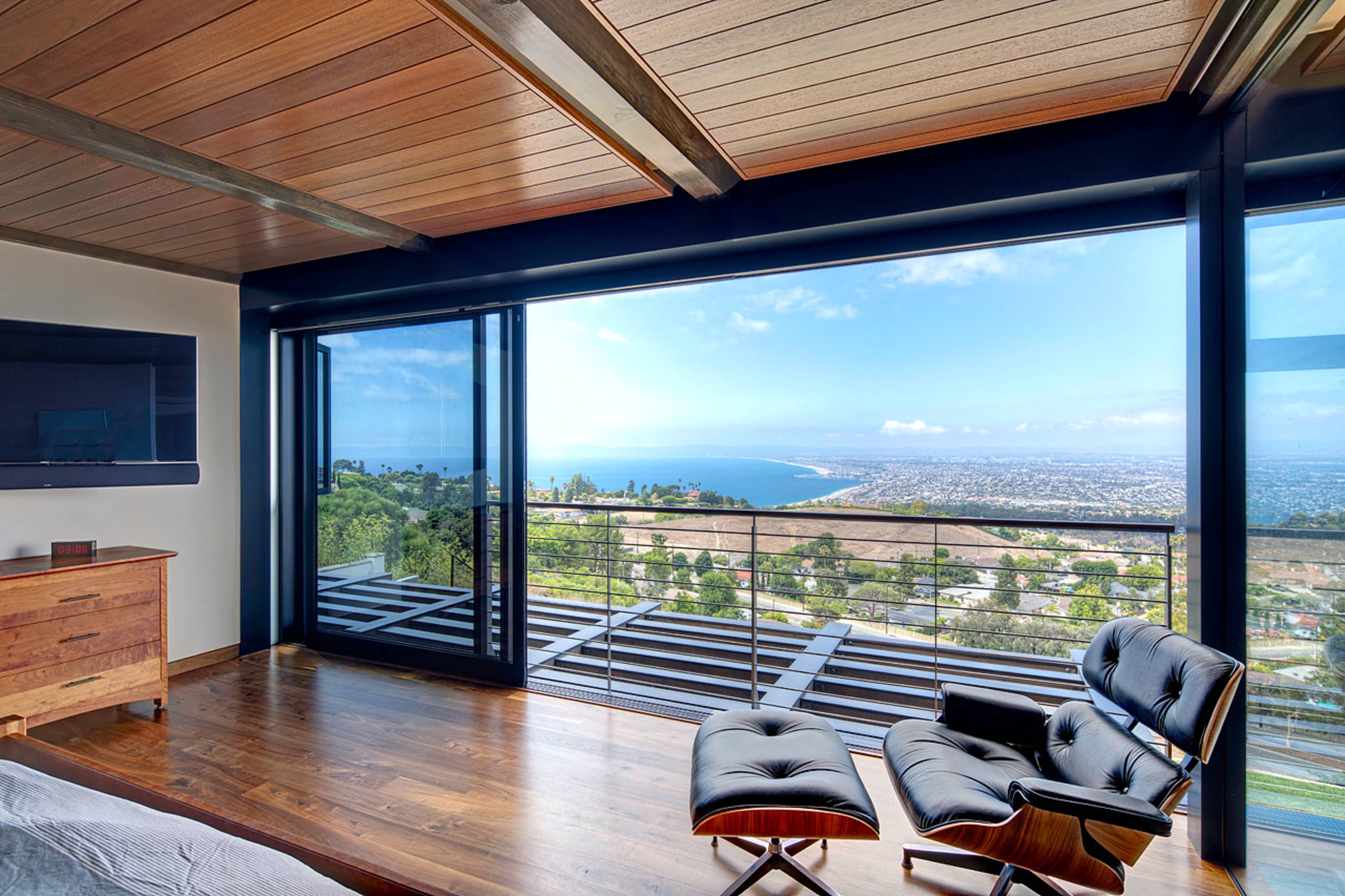 A modern bedroom with large glass windows offering a view of the ocean and surrounding landscape.