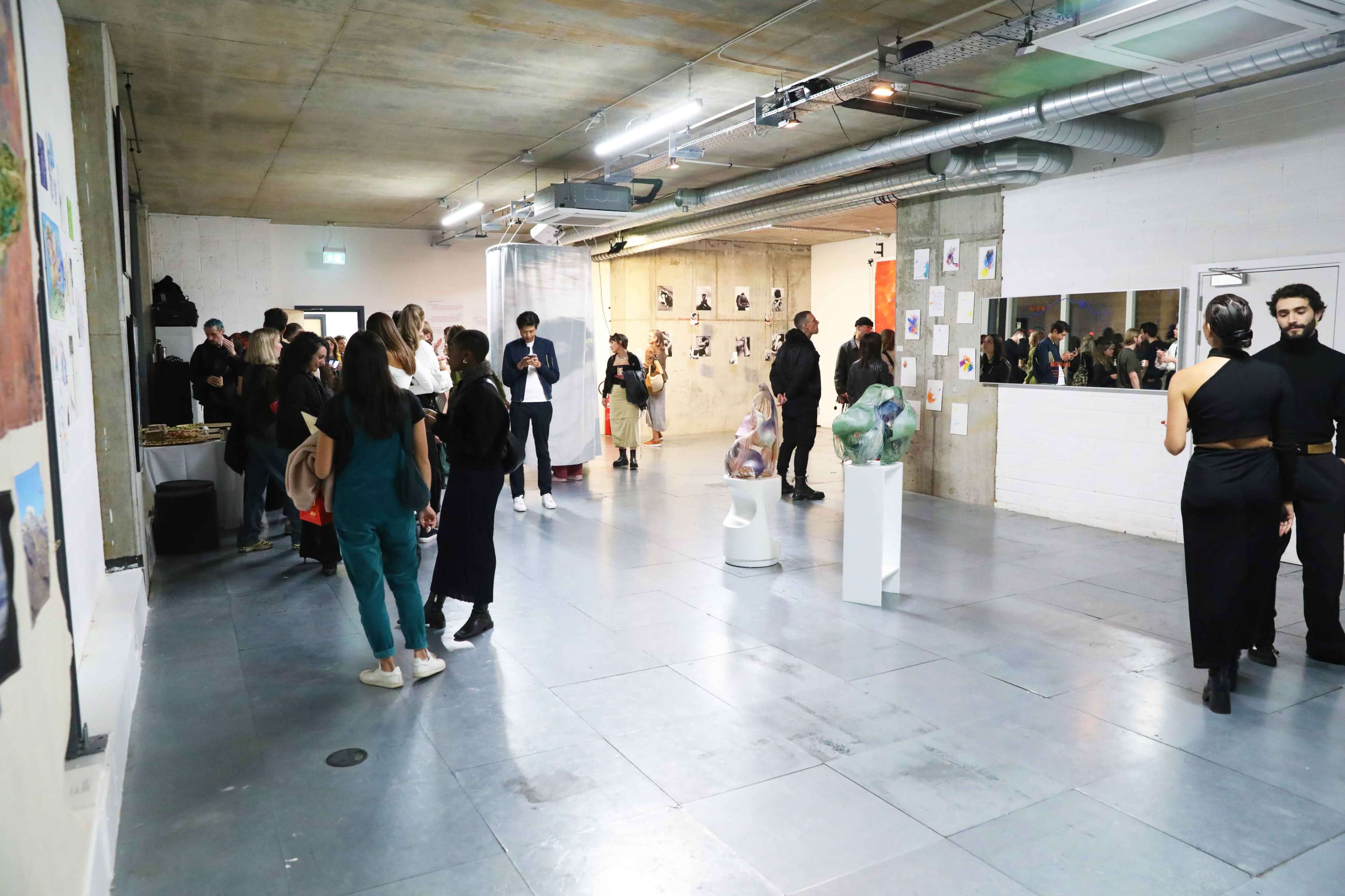 A contemporary art gallery filled with people engaging with various artworks displayed on the walls and in the center of the room.