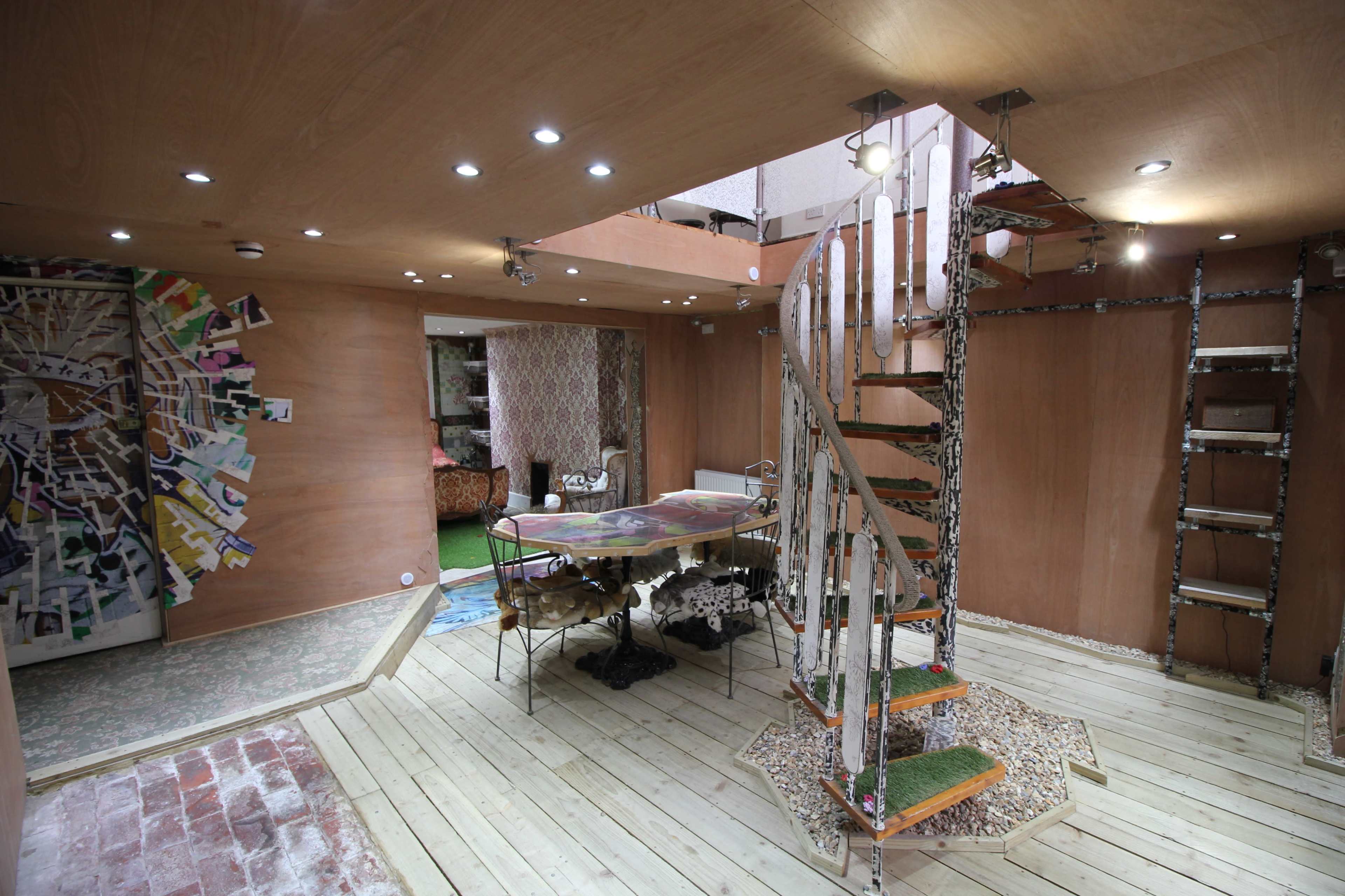 A wooden interior space featuring a spiral staircase, a decorative table, and walls decorated with various artworks.