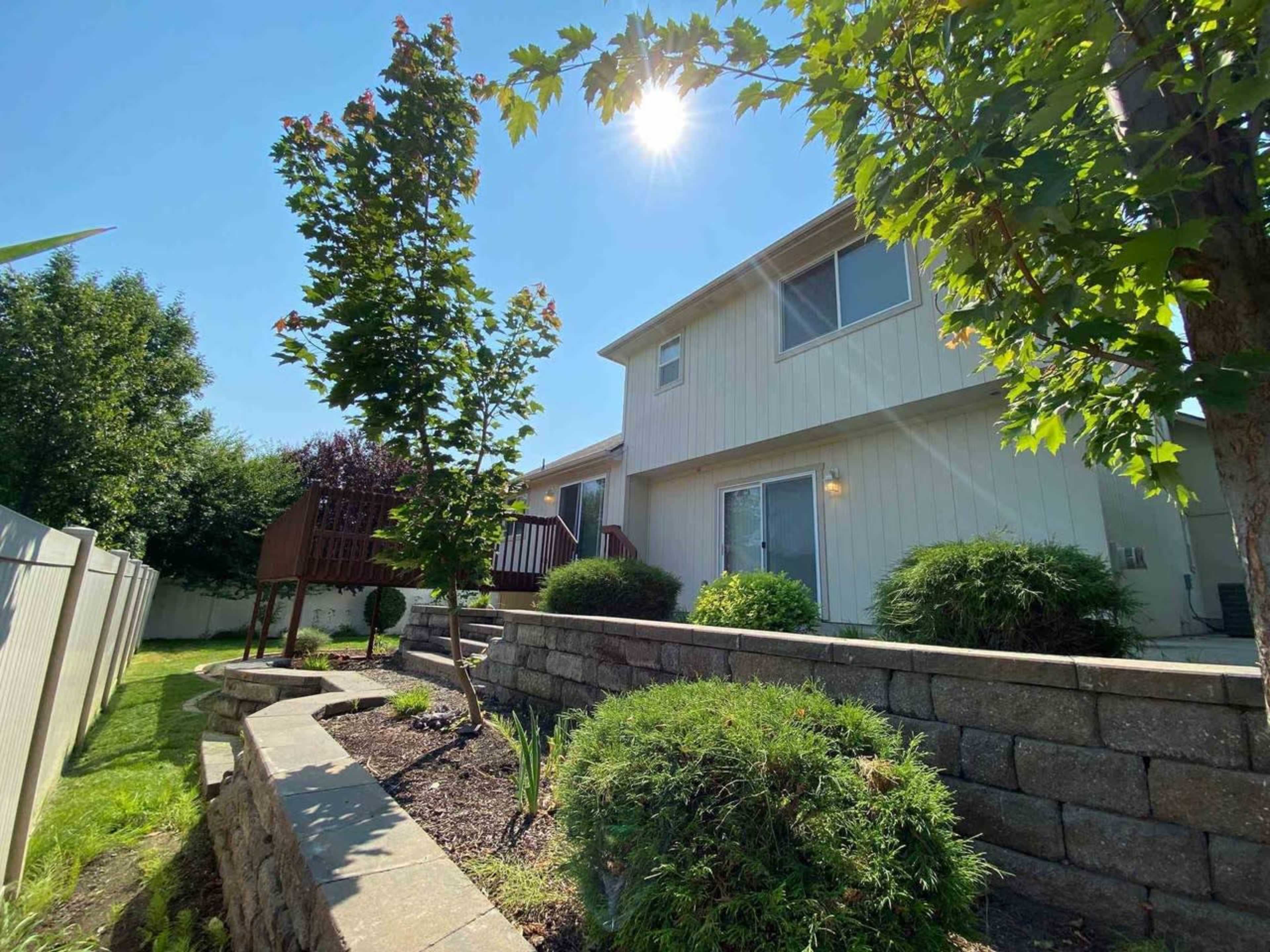 A two-story house with a landscaped yard and a wooden play structure is shown under a bright sun.