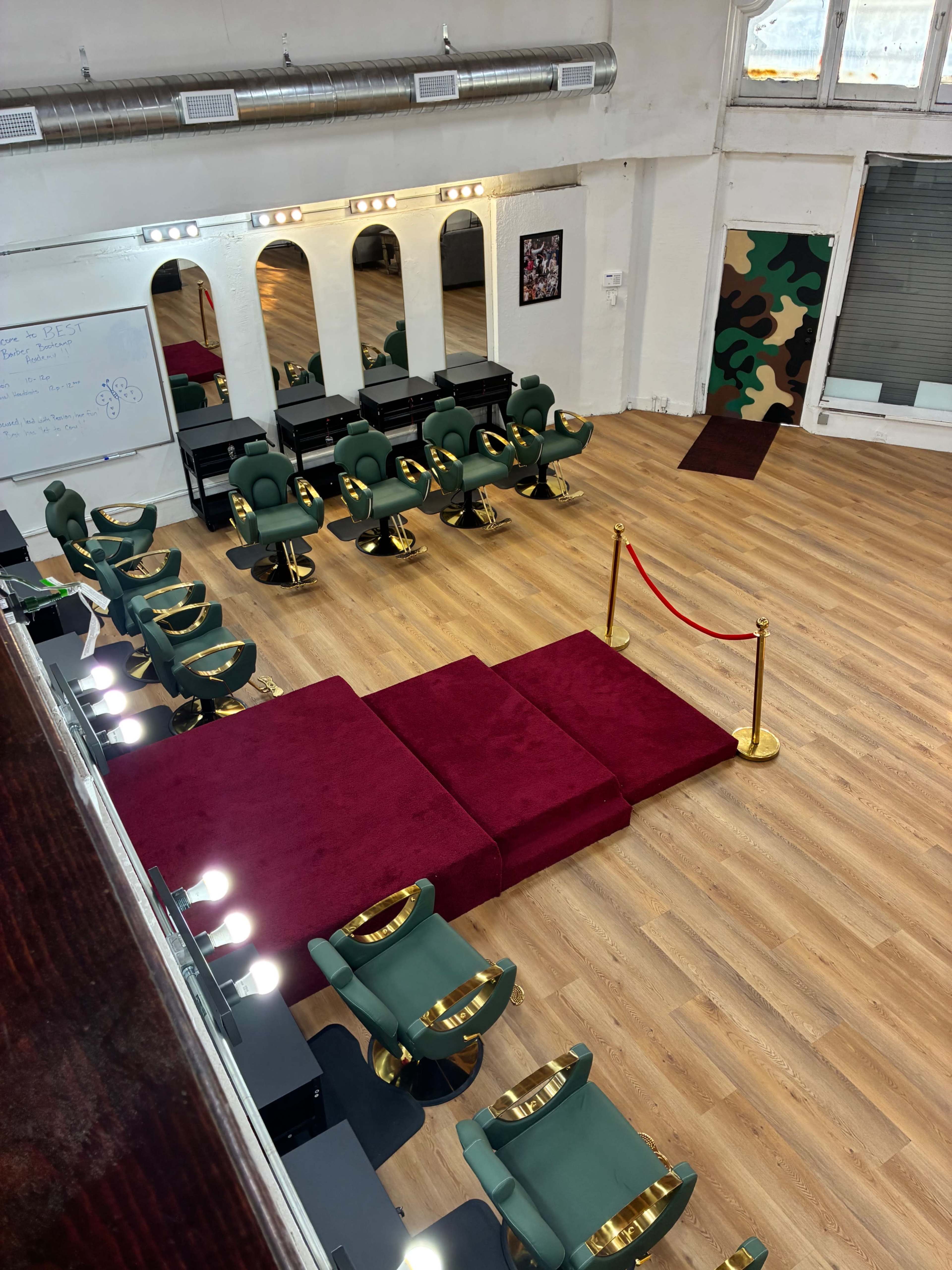 The image shows a spacious salon area with green chairs arranged in front of mirrors, a red carpet leading to a roped-off section, and wooden flooring.