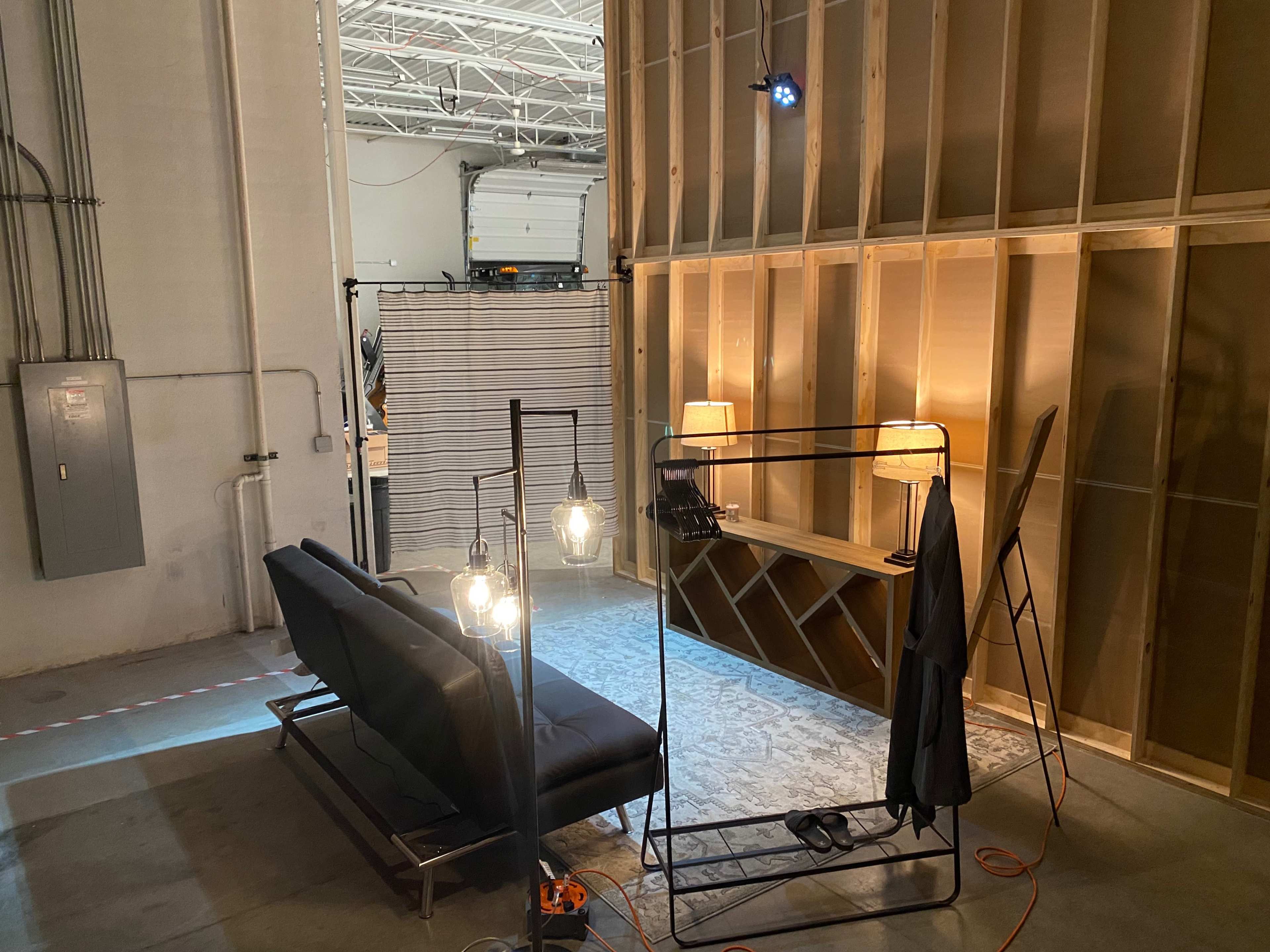 A sparsely furnished interior space with a sofa, lamps, and a backdrop of wooden walls under construction.