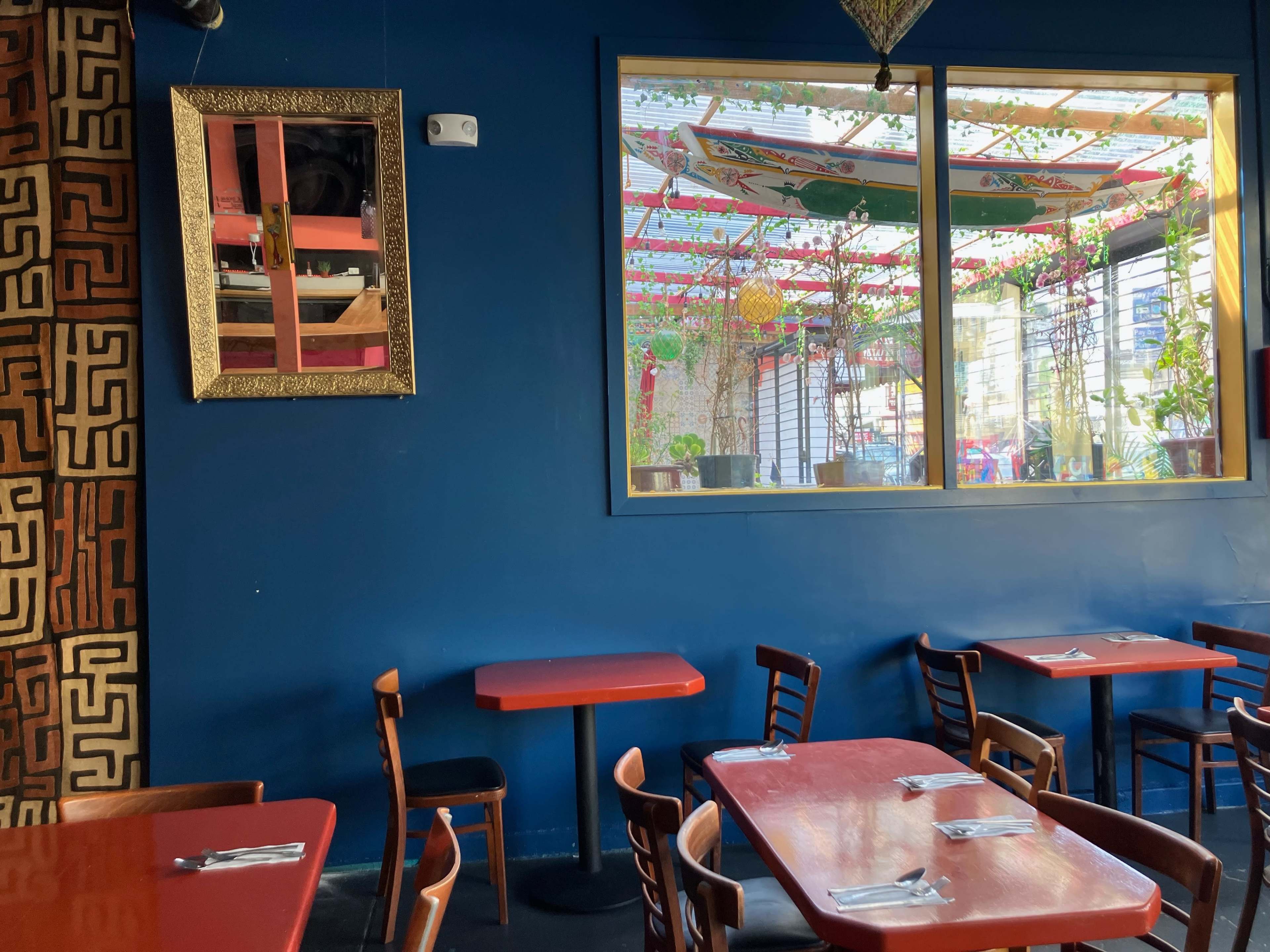 A restaurant interior with red tables and wooden chairs, featuring a large window that reveals a colorful outdoor area.
