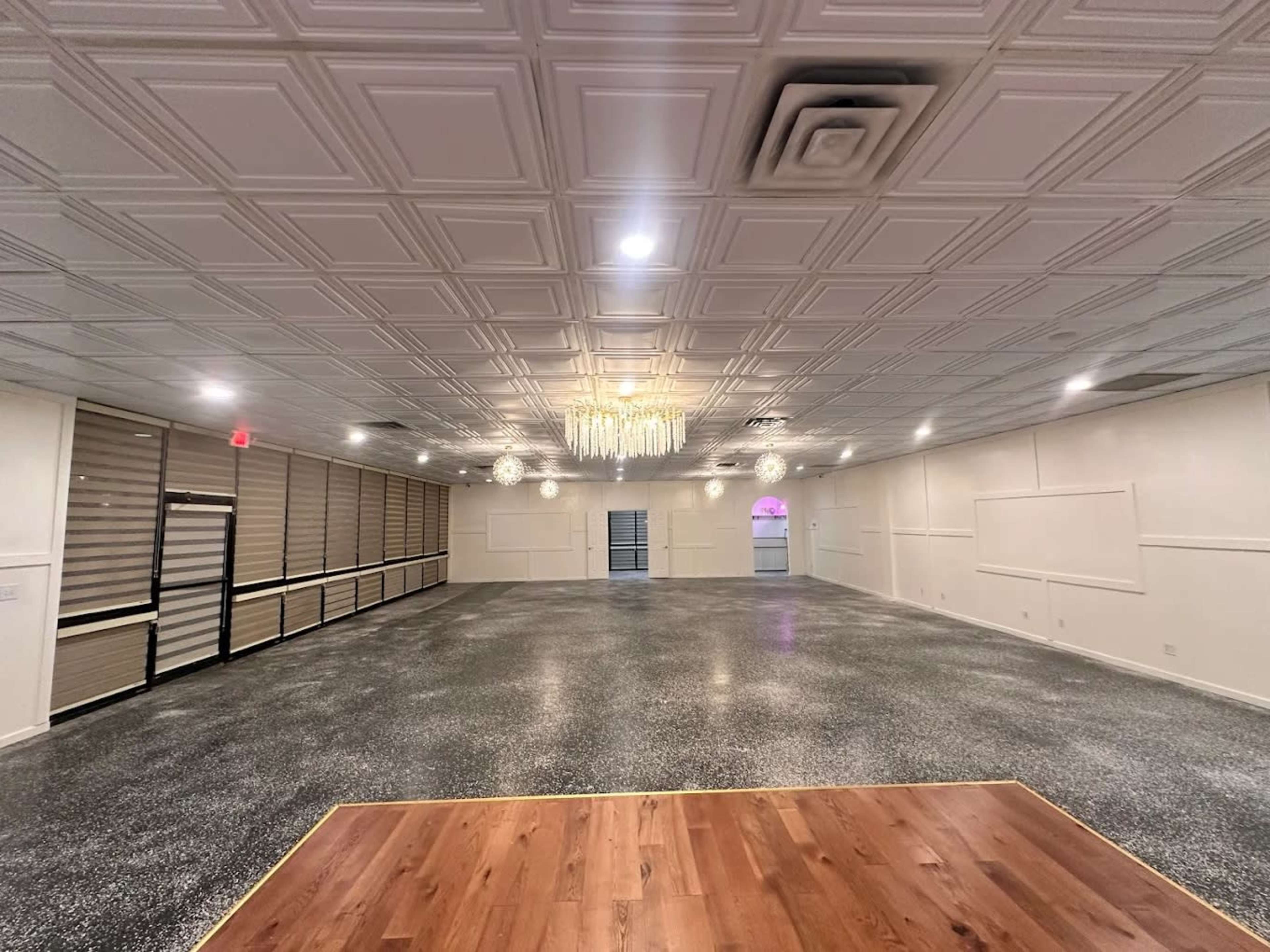 The image shows a spacious interior with a polished concrete floor, bright ceiling lights, and a decorative ceiling, featuring a large open area suitable for events.