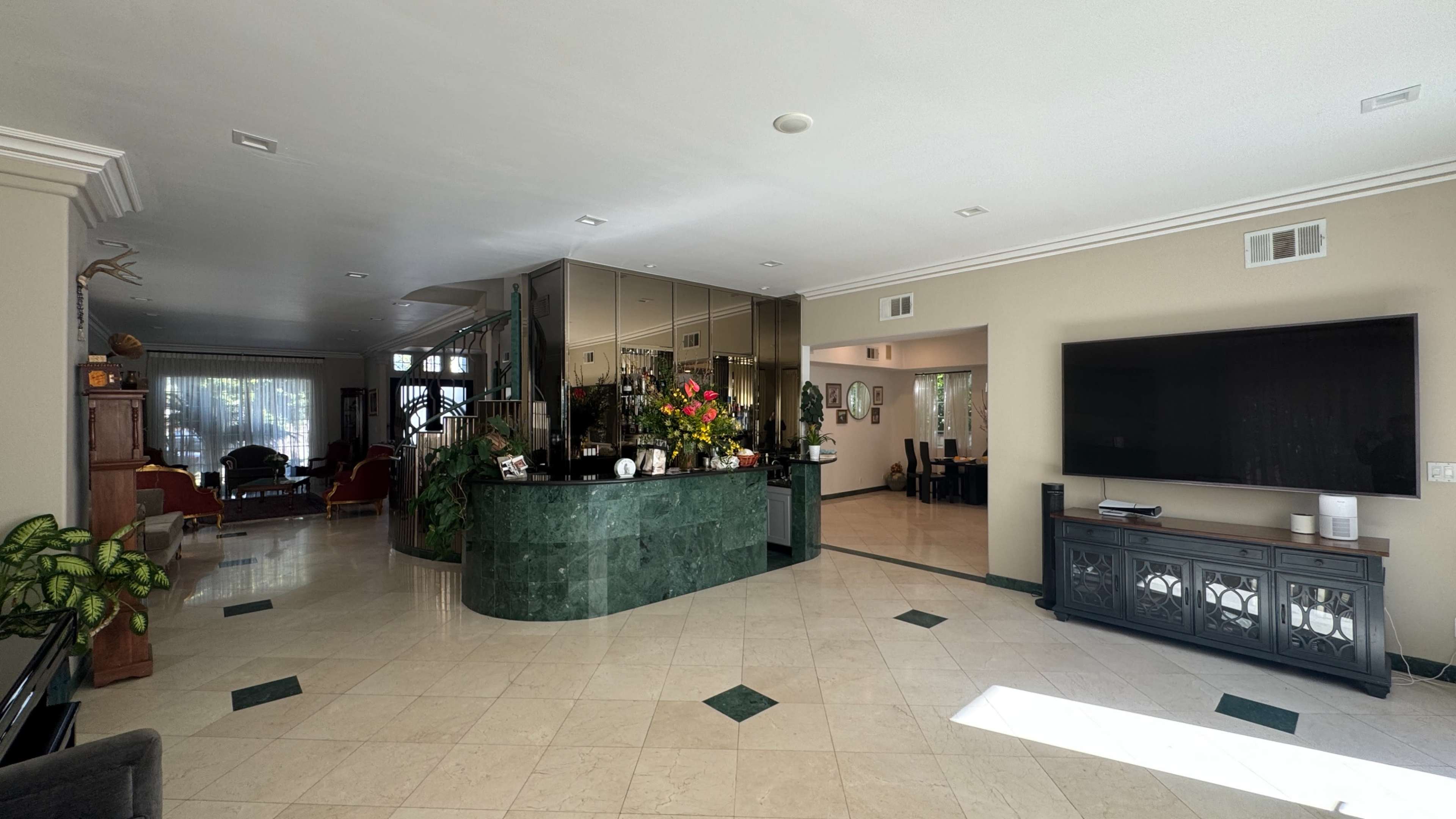 The image shows an open living space featuring a bar area with a green marble countertop, tiled floors, and adjacent seating and dining areas.