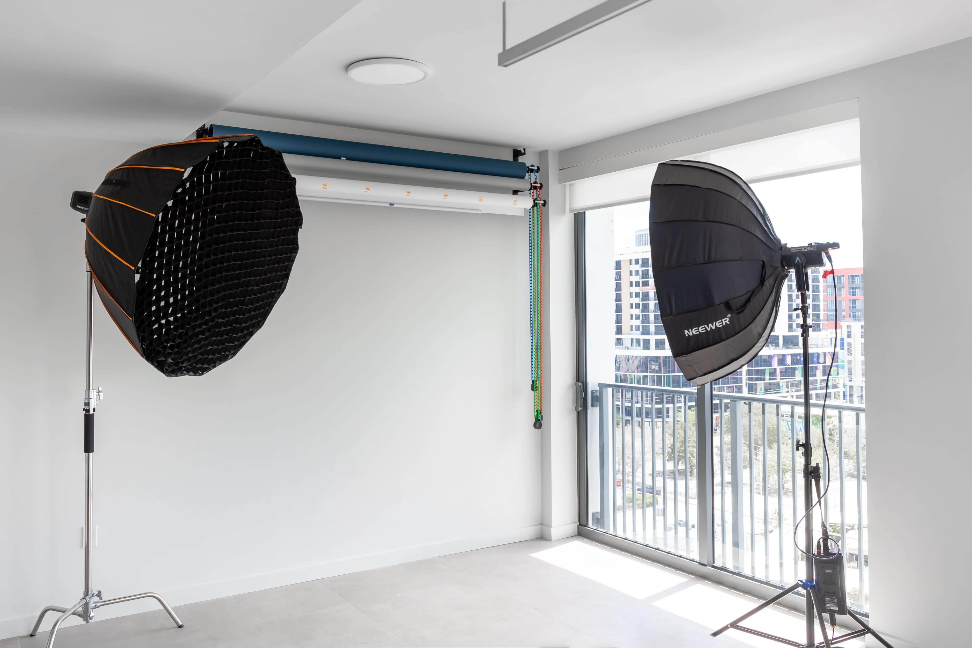 The image shows a photography studio setup with two light softboxes positioned near a window, and a backdrop support system mounted on the wall.