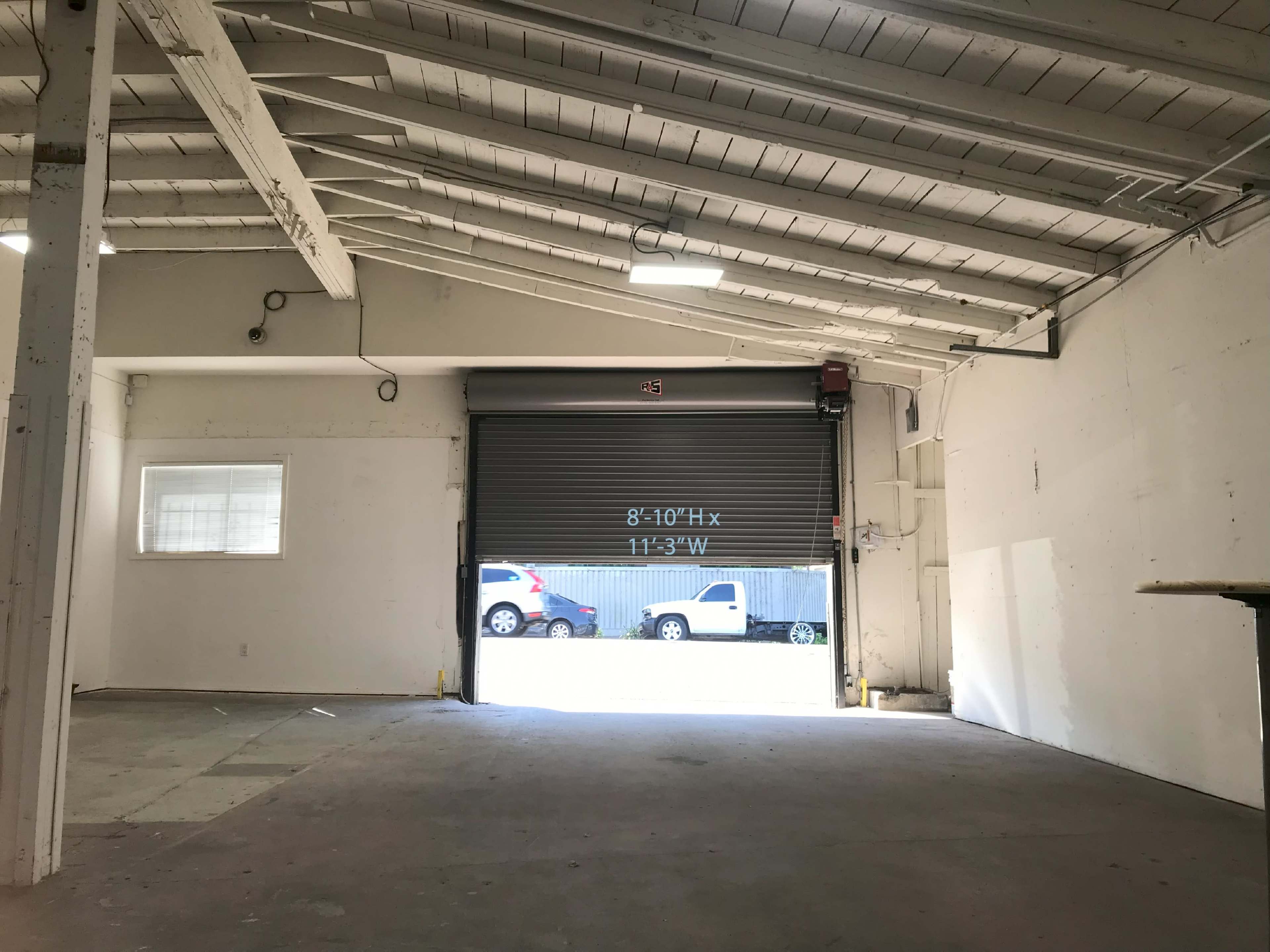 The interior of a spacious warehouse features a roll-up door and a concrete floor.