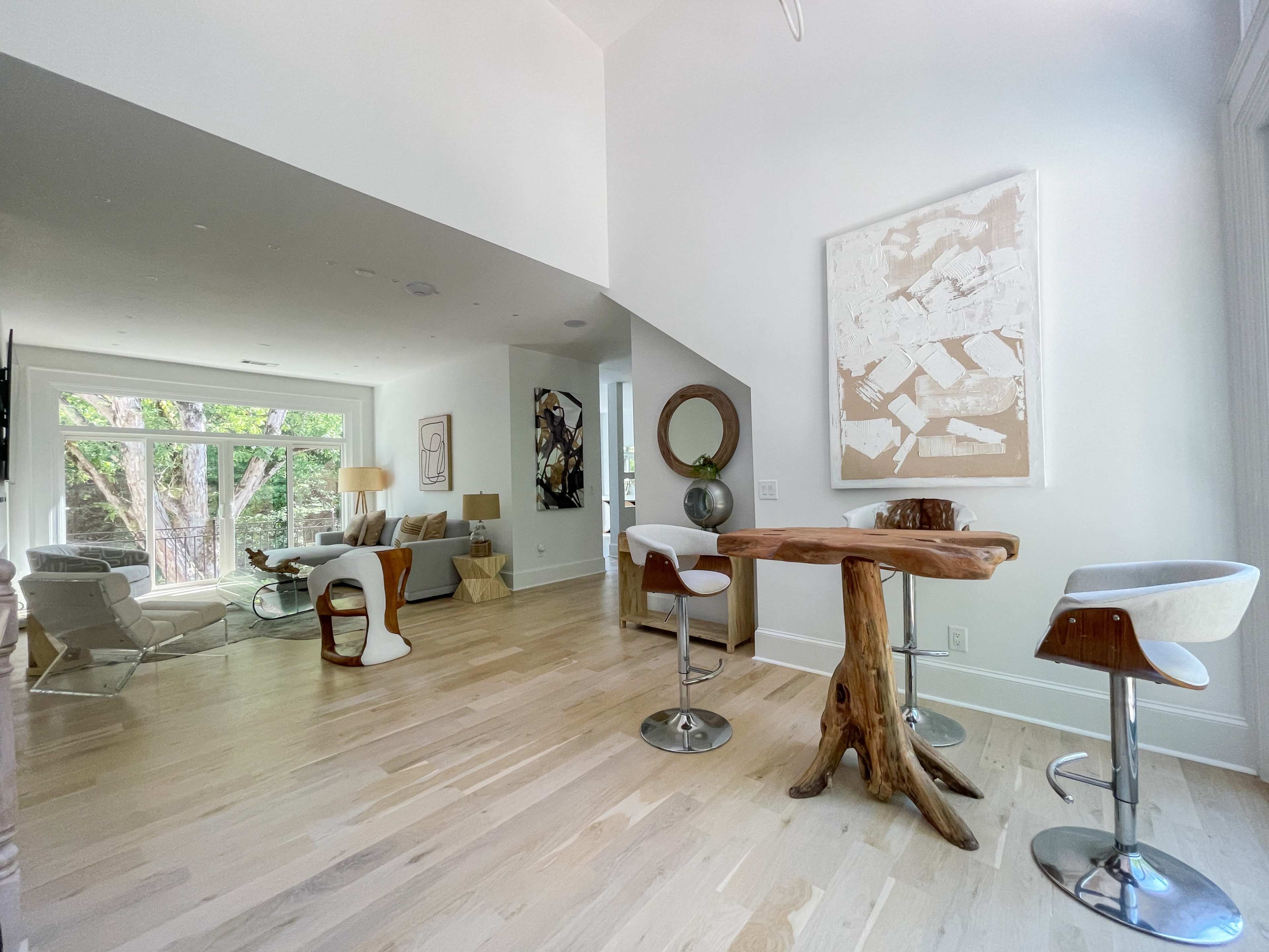 The scene shows a modern interior space featuring a seating area with large windows, a small wooden table, and contemporary chairs.
