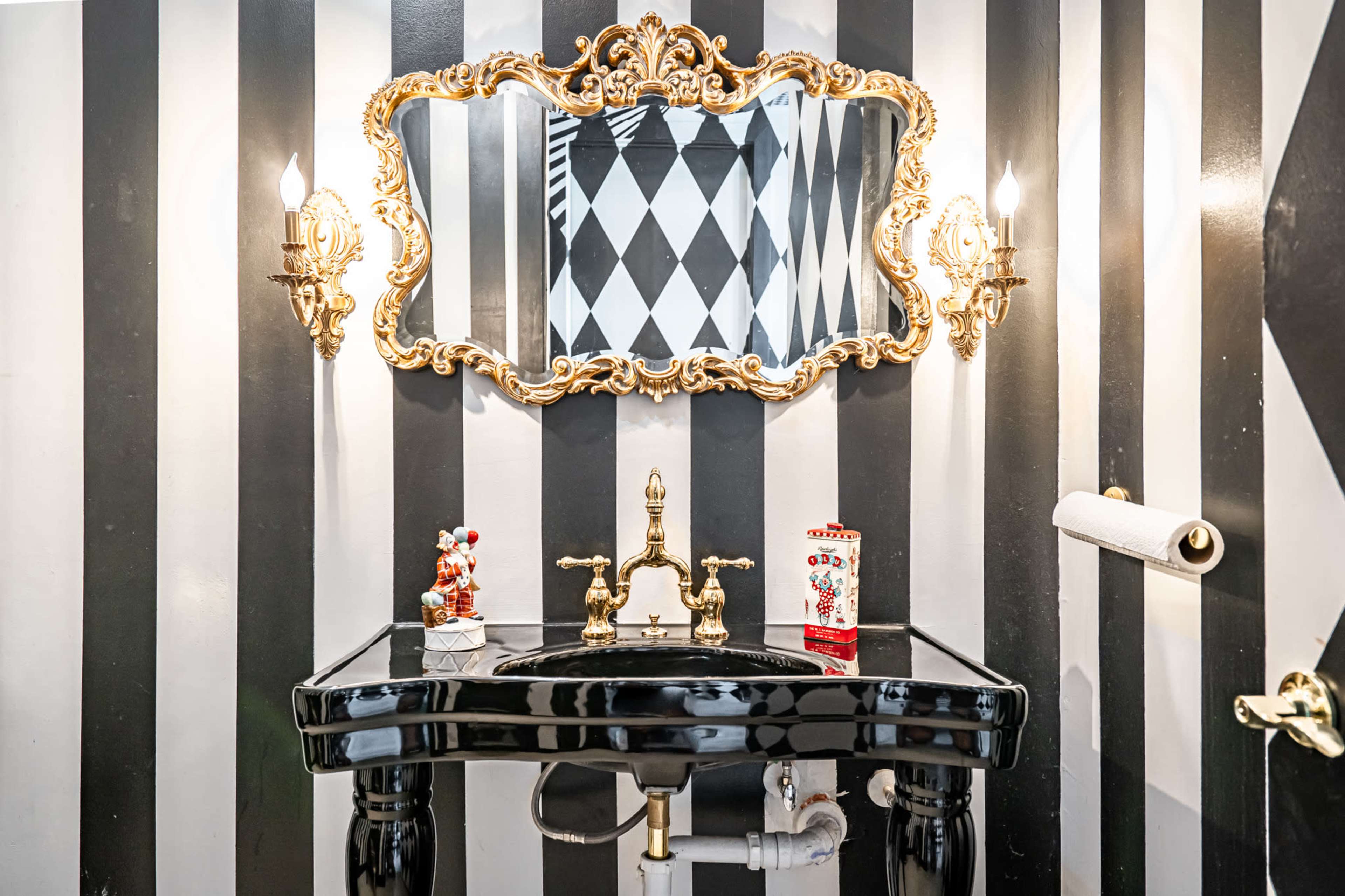 A black and white striped bathroom featuring a baroque-style mirror and a sleek, black sink with gold fixtures.