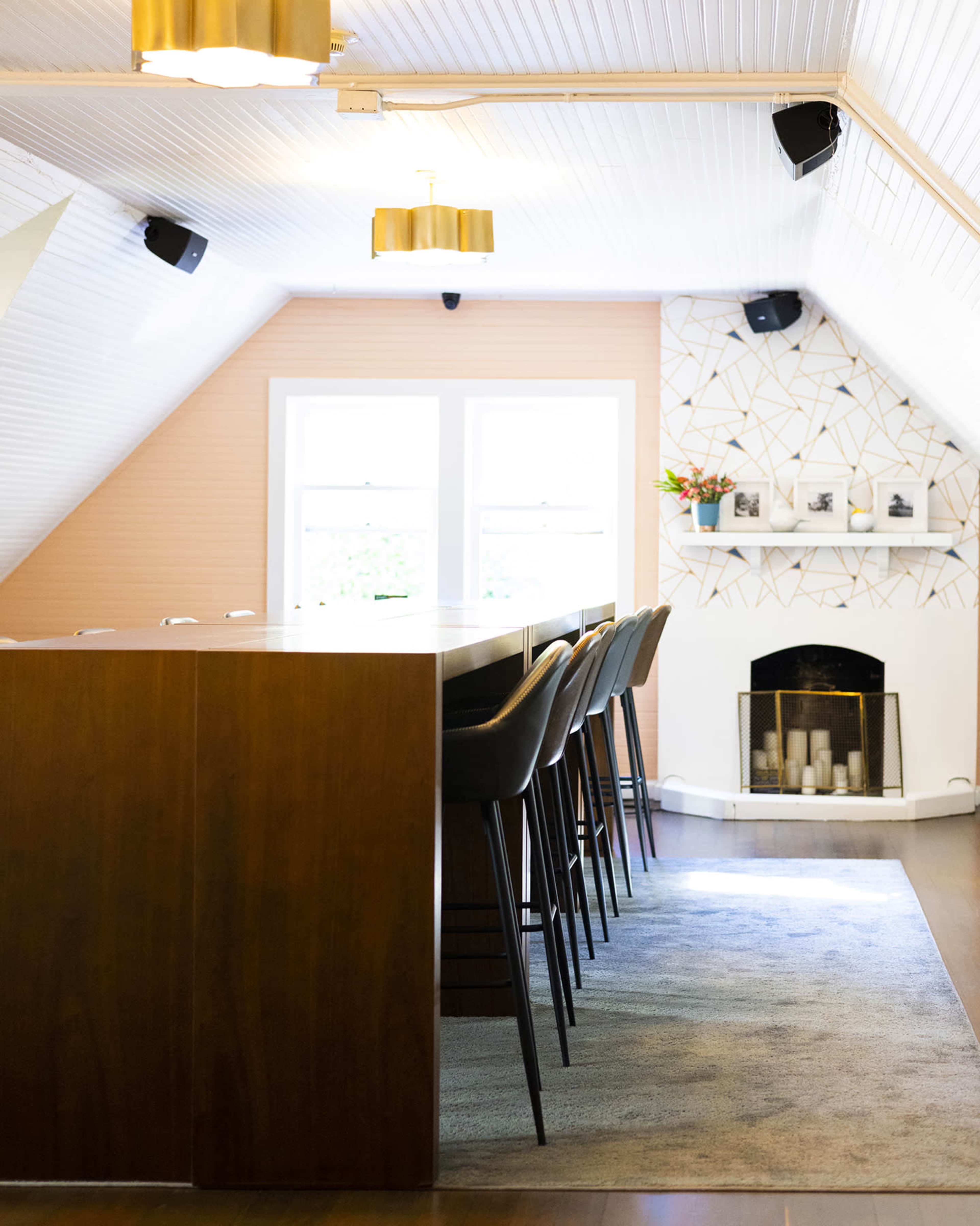 The image shows a modern kitchen with a wooden island and bar stools, set in an attic-like space with sloped ceilings and decorative wall accents.