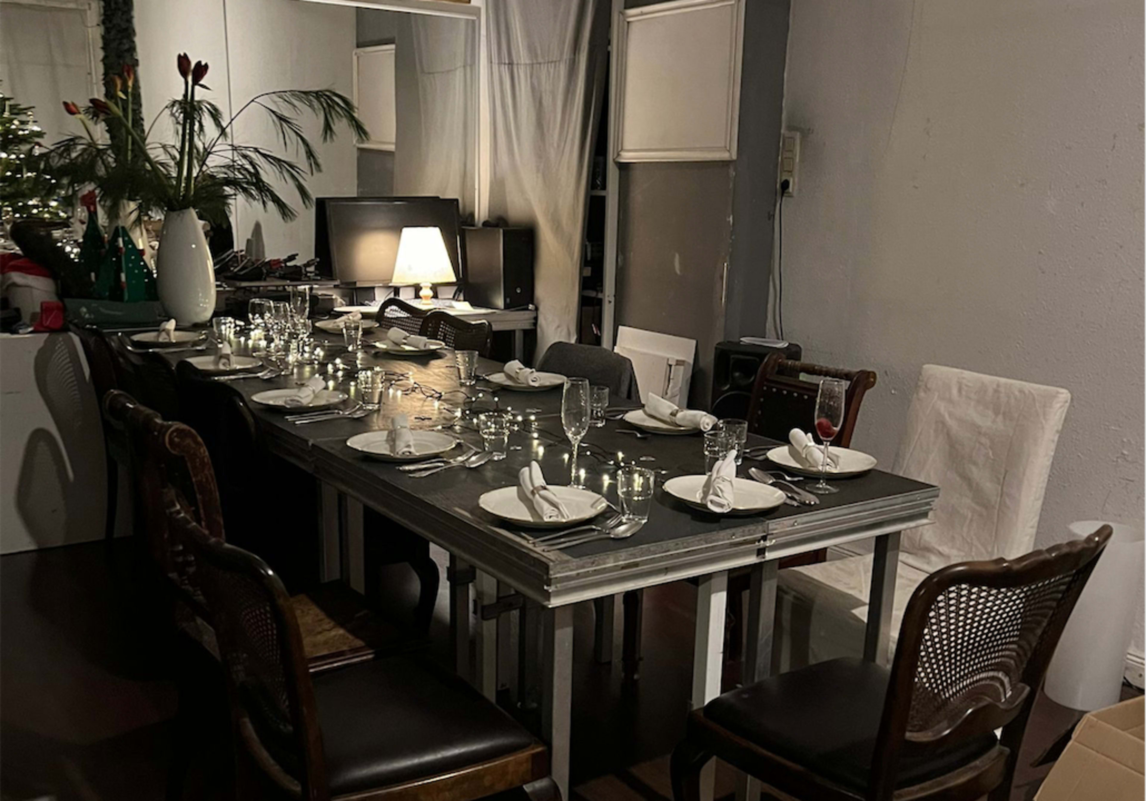 A long dining table is set with plates, glassware, and silverware, surrounded by chairs in a softly lit room.