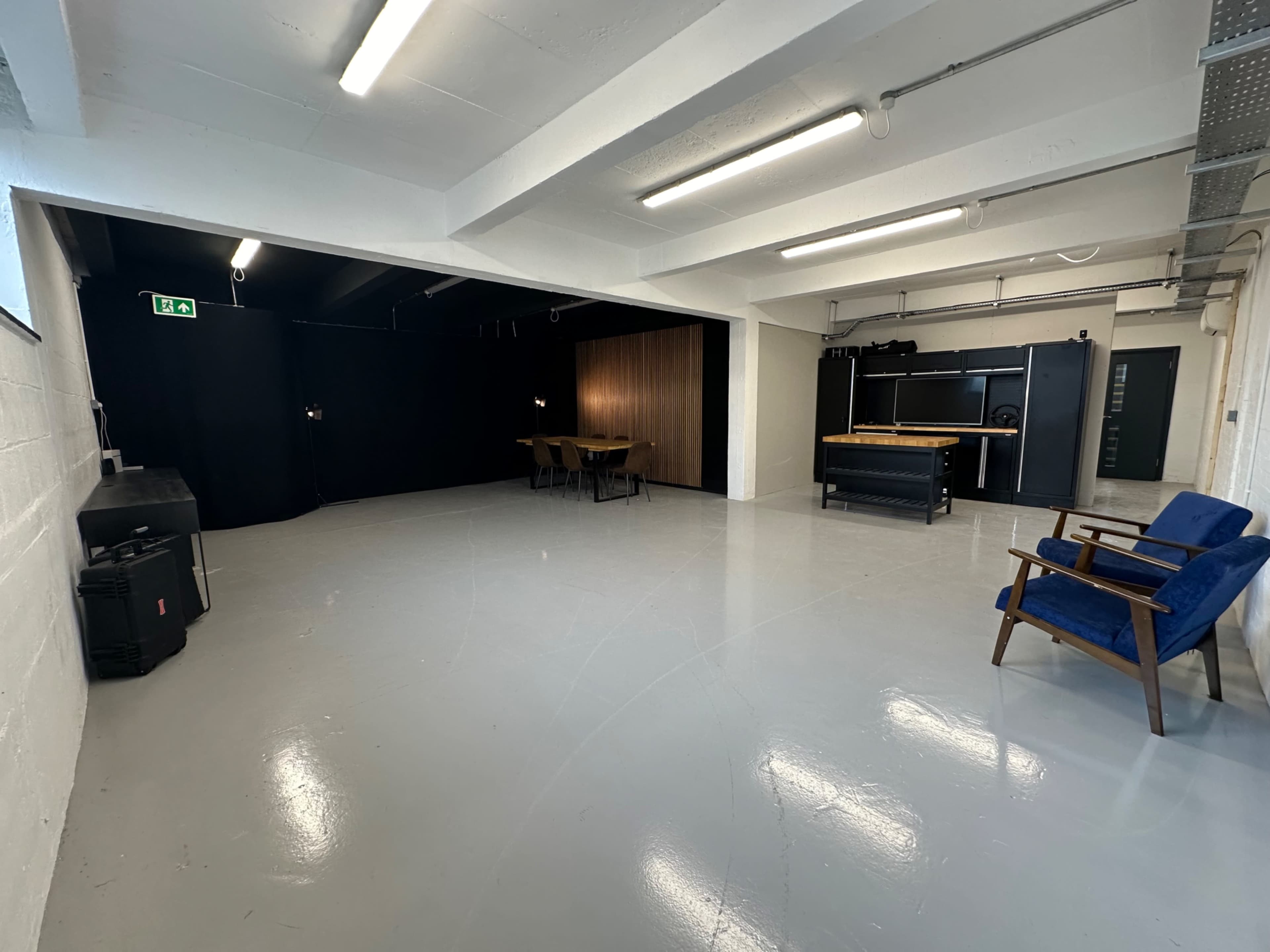 A spacious, empty room with a polished white floor, featuring a seating area on one side and a table with chairs on the other side, separated by a black backdrop.