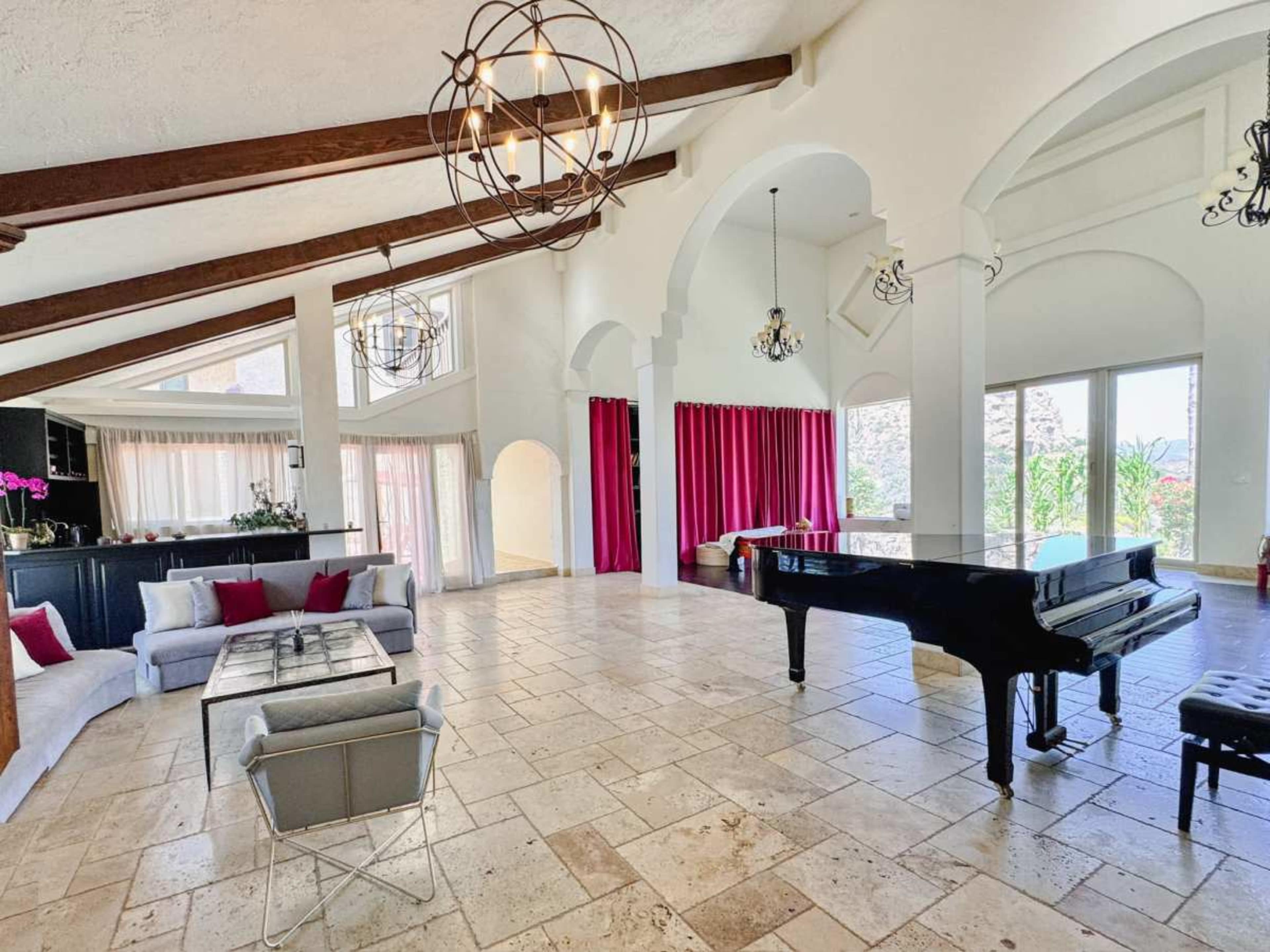 The spacious room features high ceilings, a grand piano, and large windows with pink curtains.
