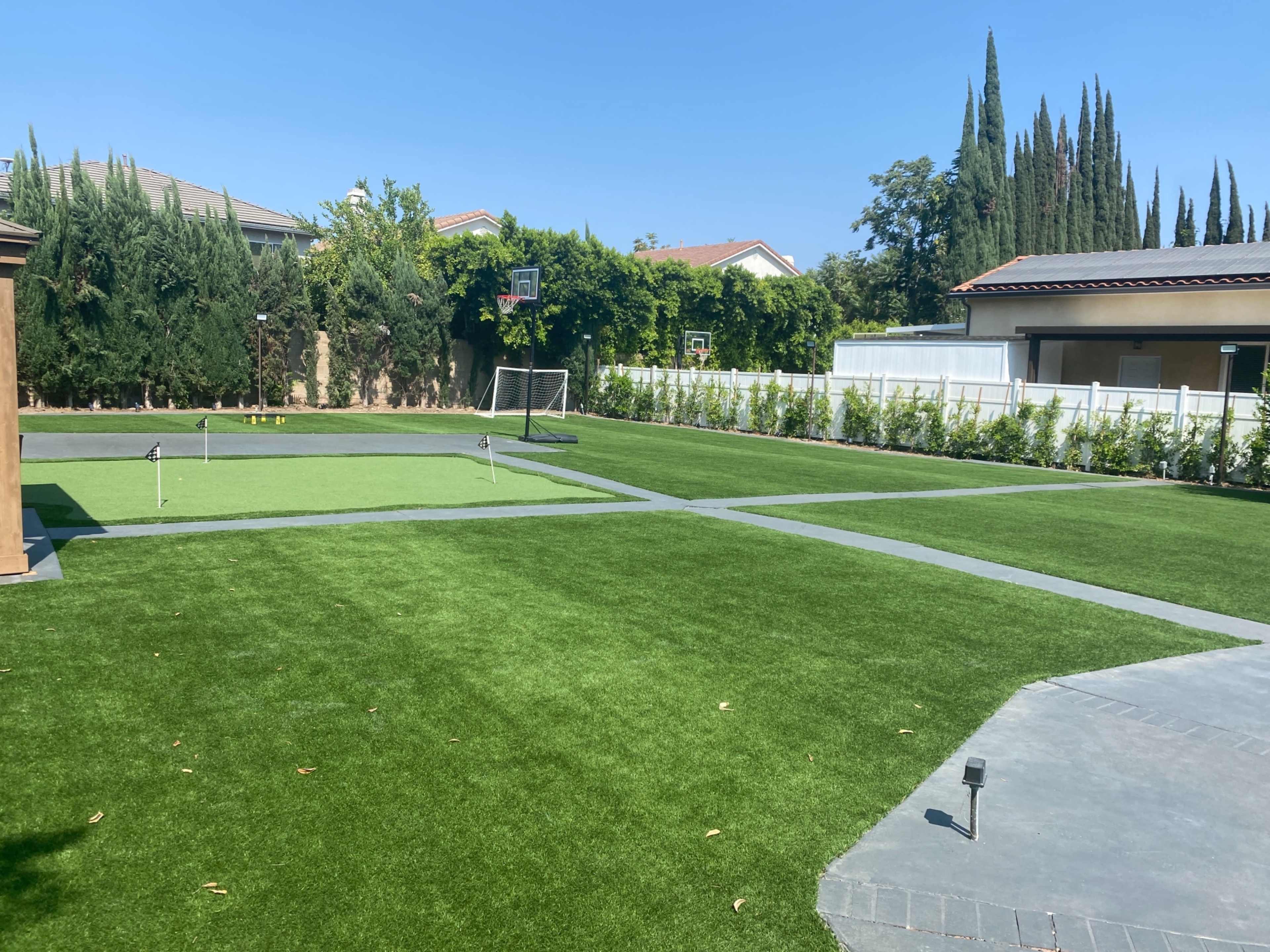 A spacious backyard featuring artificial turf, a basketball hoop, a soccer goal, and several trees along the perimeter.