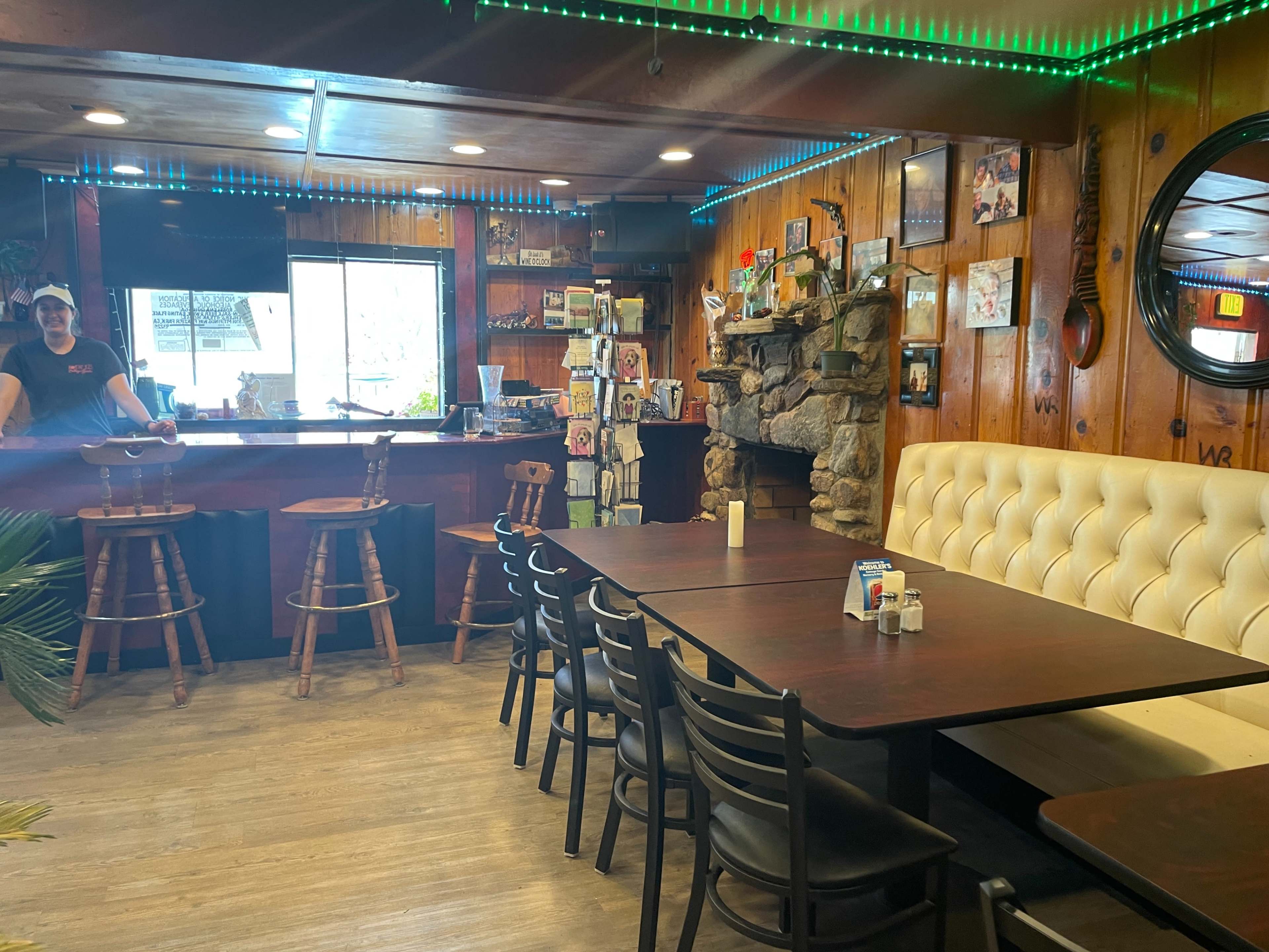 The interior of a rustic restaurant with wooden paneling, a bar area, and several tables arranged for dining.
