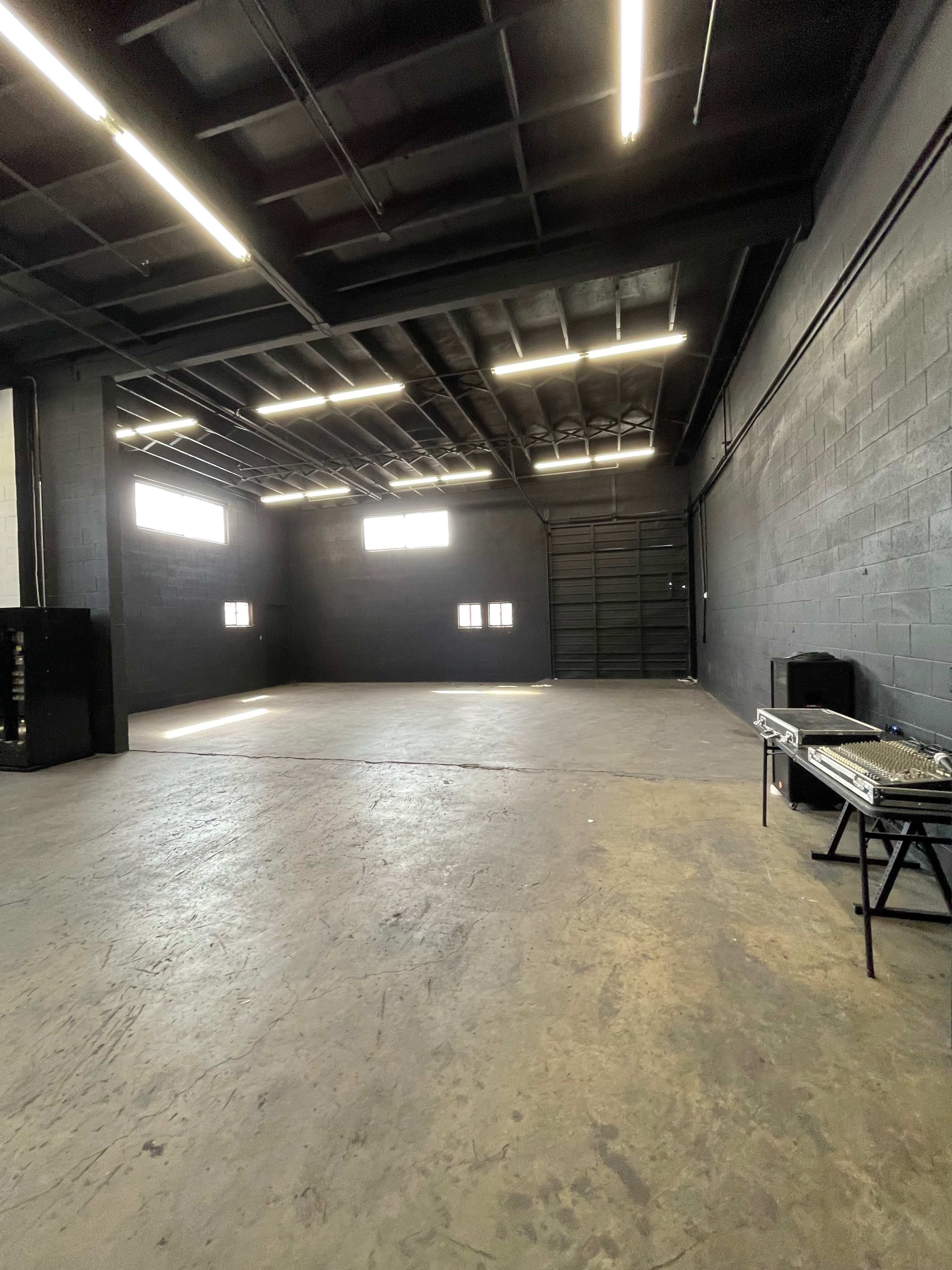 A large, empty industrial space with black walls and a concrete floor, illuminated by overhead lighting.