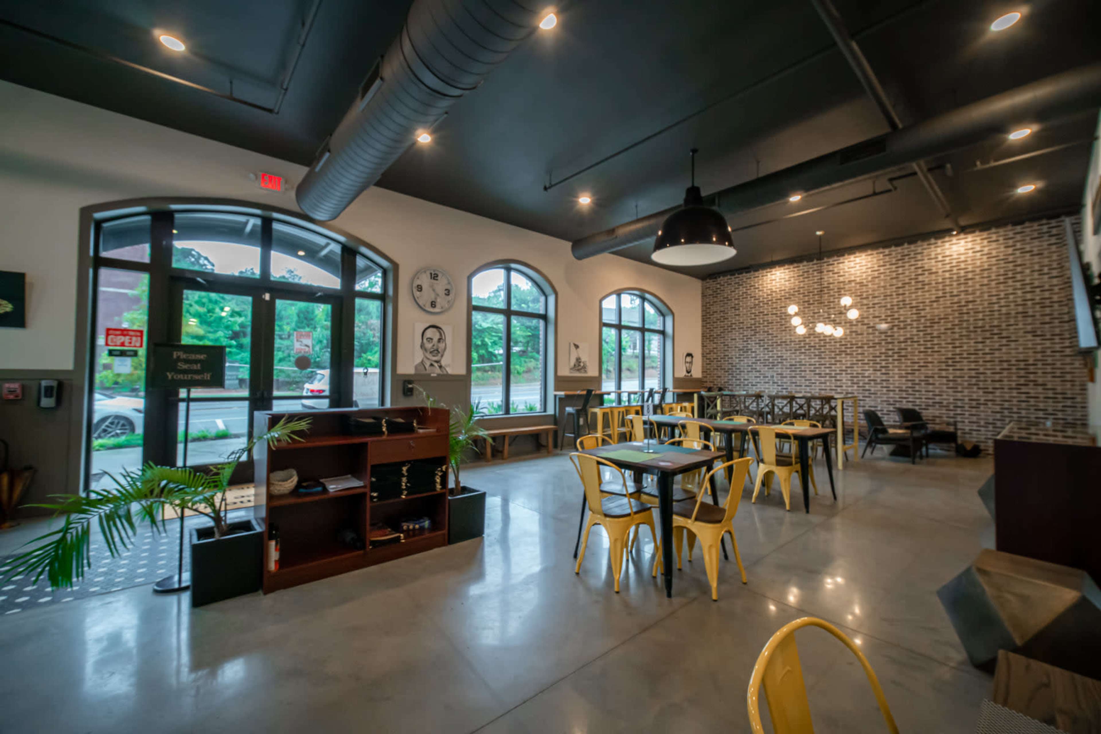 A modern café interior with industrial-style decor, featuring yellow chairs, wooden tables, and large windows allowing natural light to enter.