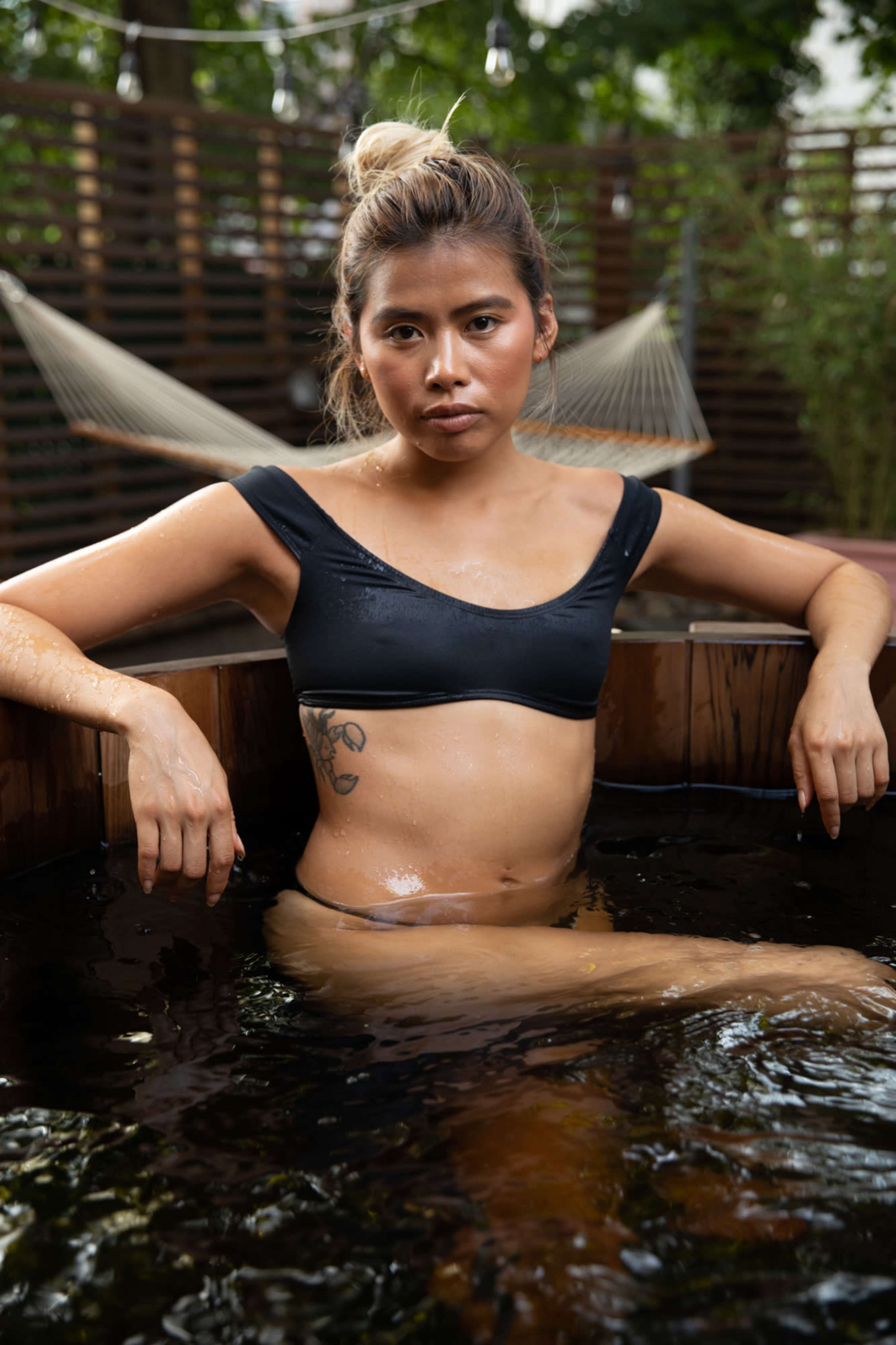 A person sits in a wooden hot tub with a hammock in the background.