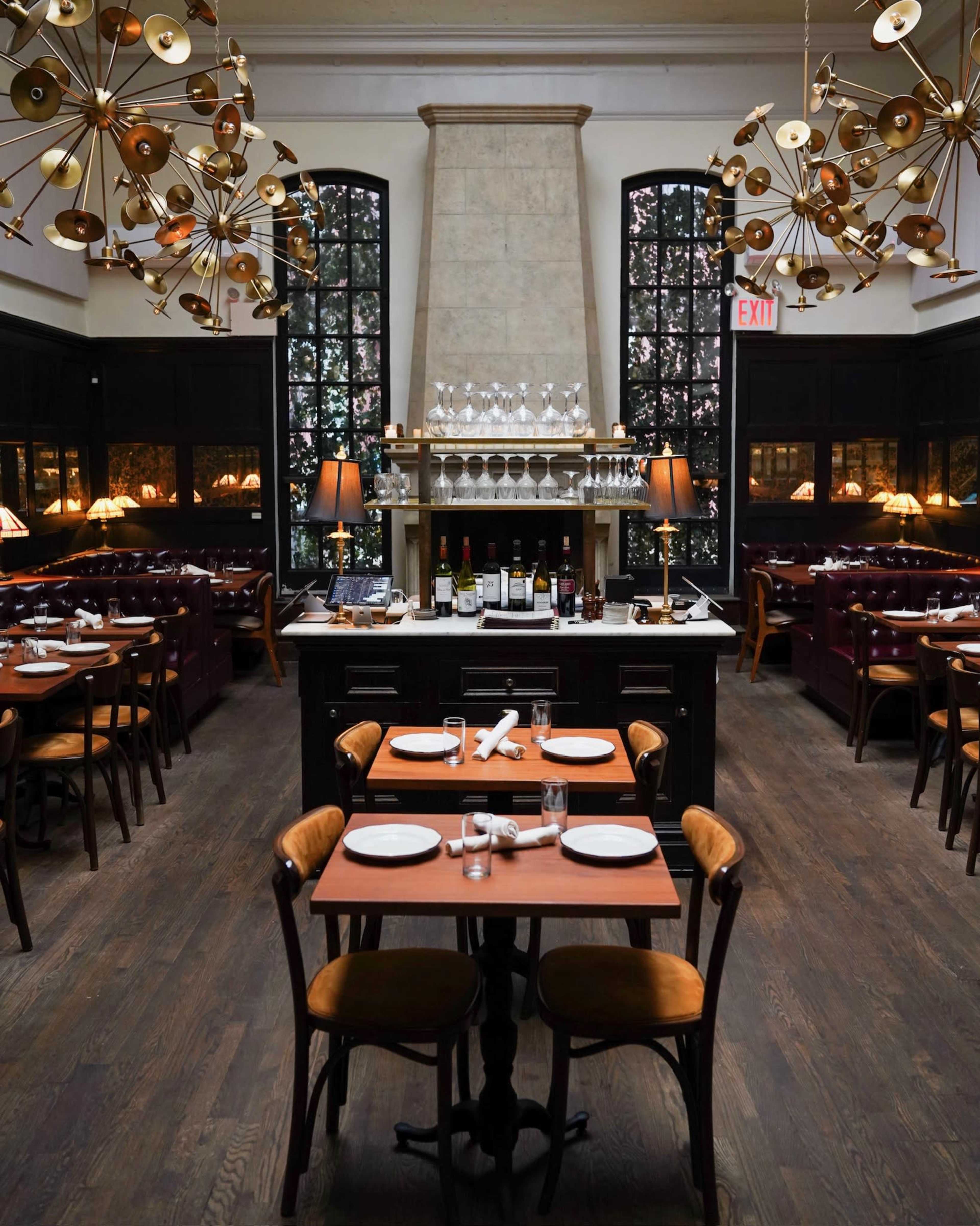 A stylish restaurant interior with wooden floors, tables set for dining, and elegant light fixtures hanging from the ceiling.