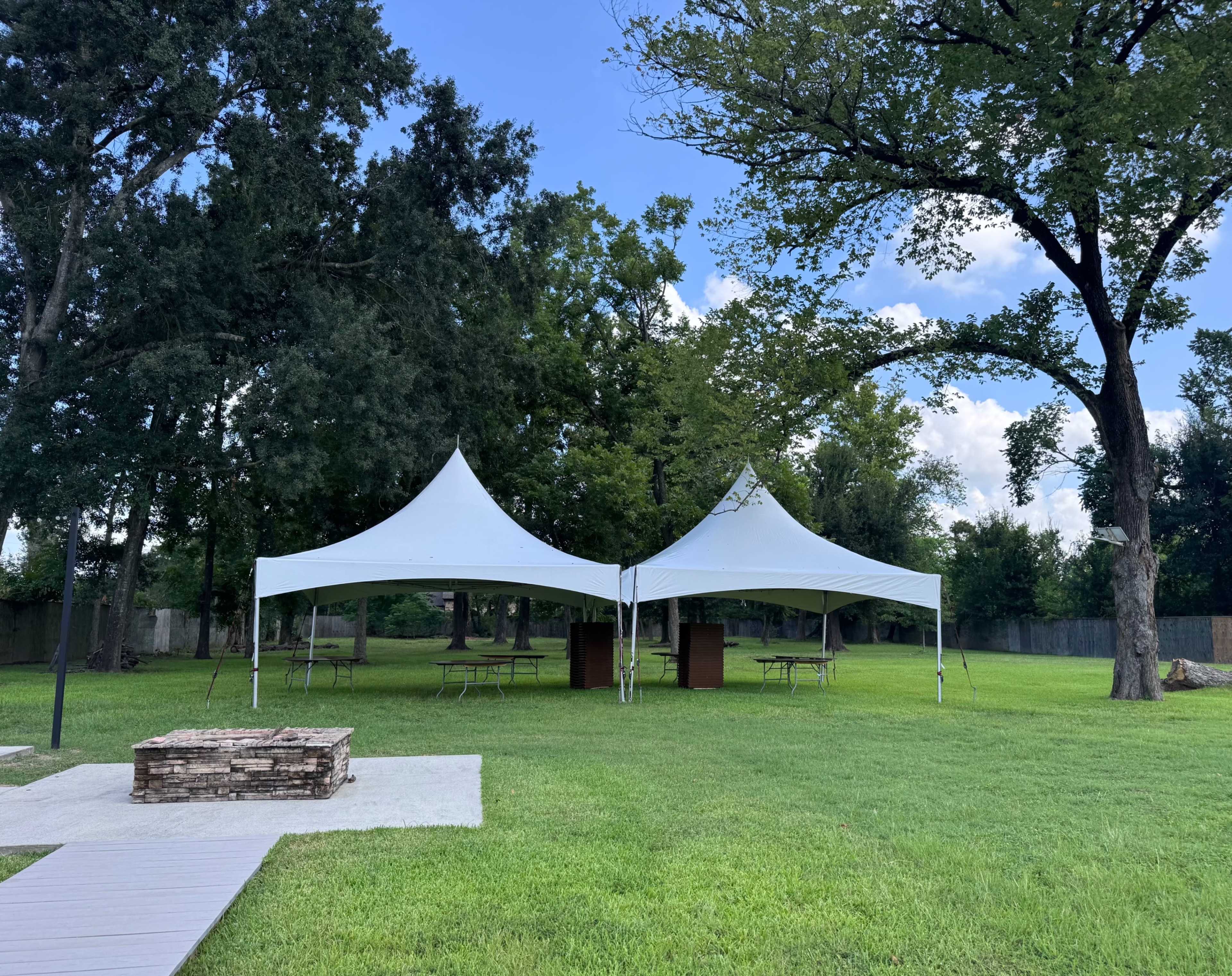 Two white canopies are set up on a grassy area surrounded by trees.