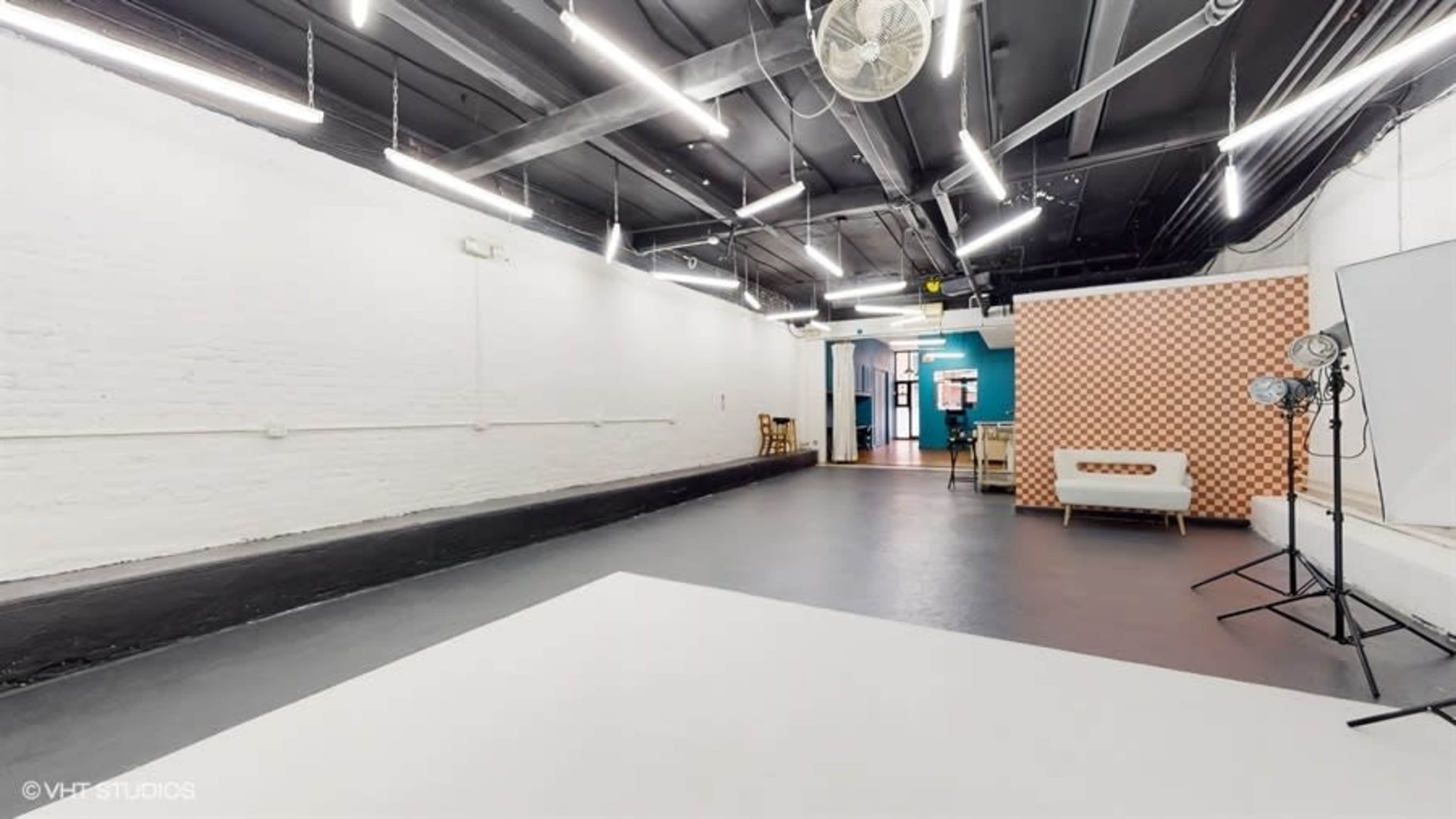 A spacious, well-lit studio with white walls, a black floor, and a seating area in the background.