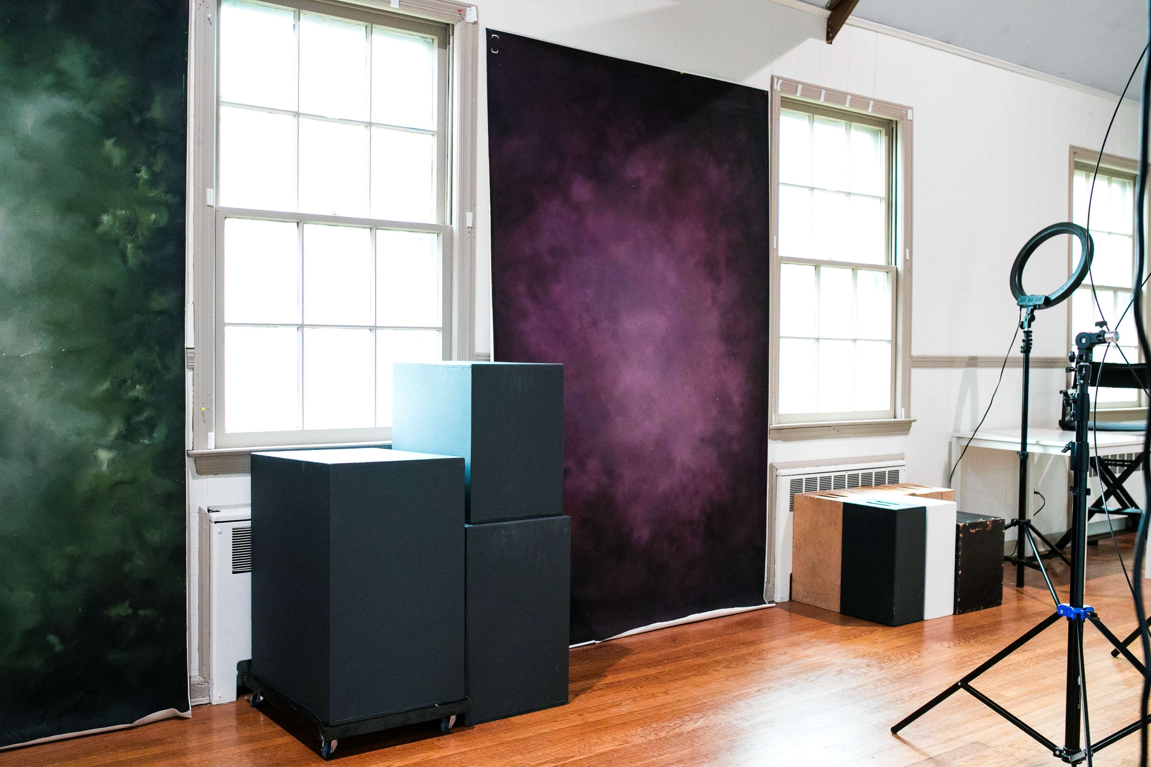 A room with green and purple backdrops, stacked black and brown boxes, and a photography ring light set up.