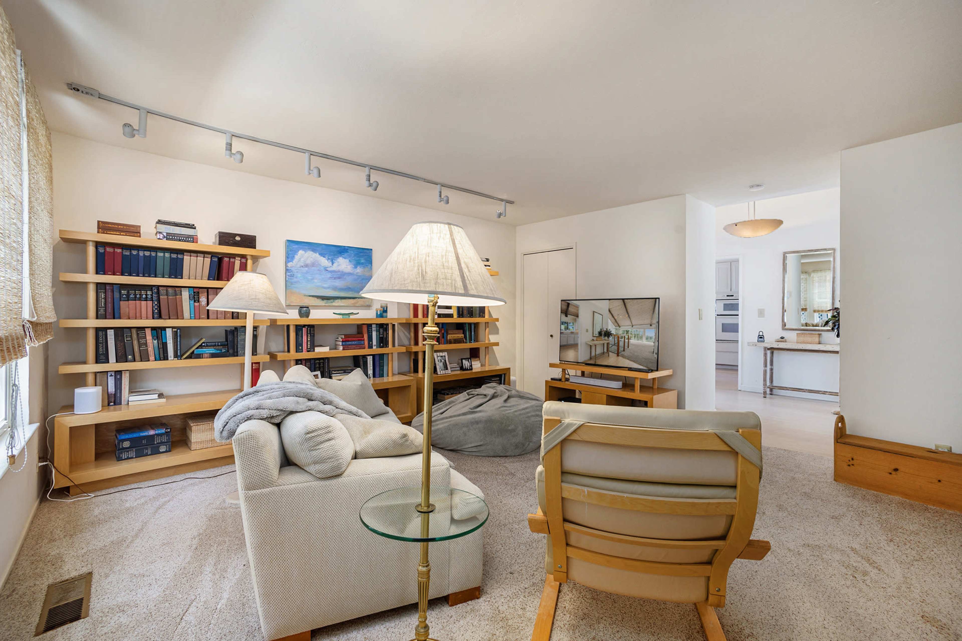 A cozy living room features a television, bookshelf filled with books, and comfortable seating with lamps illuminating the space.