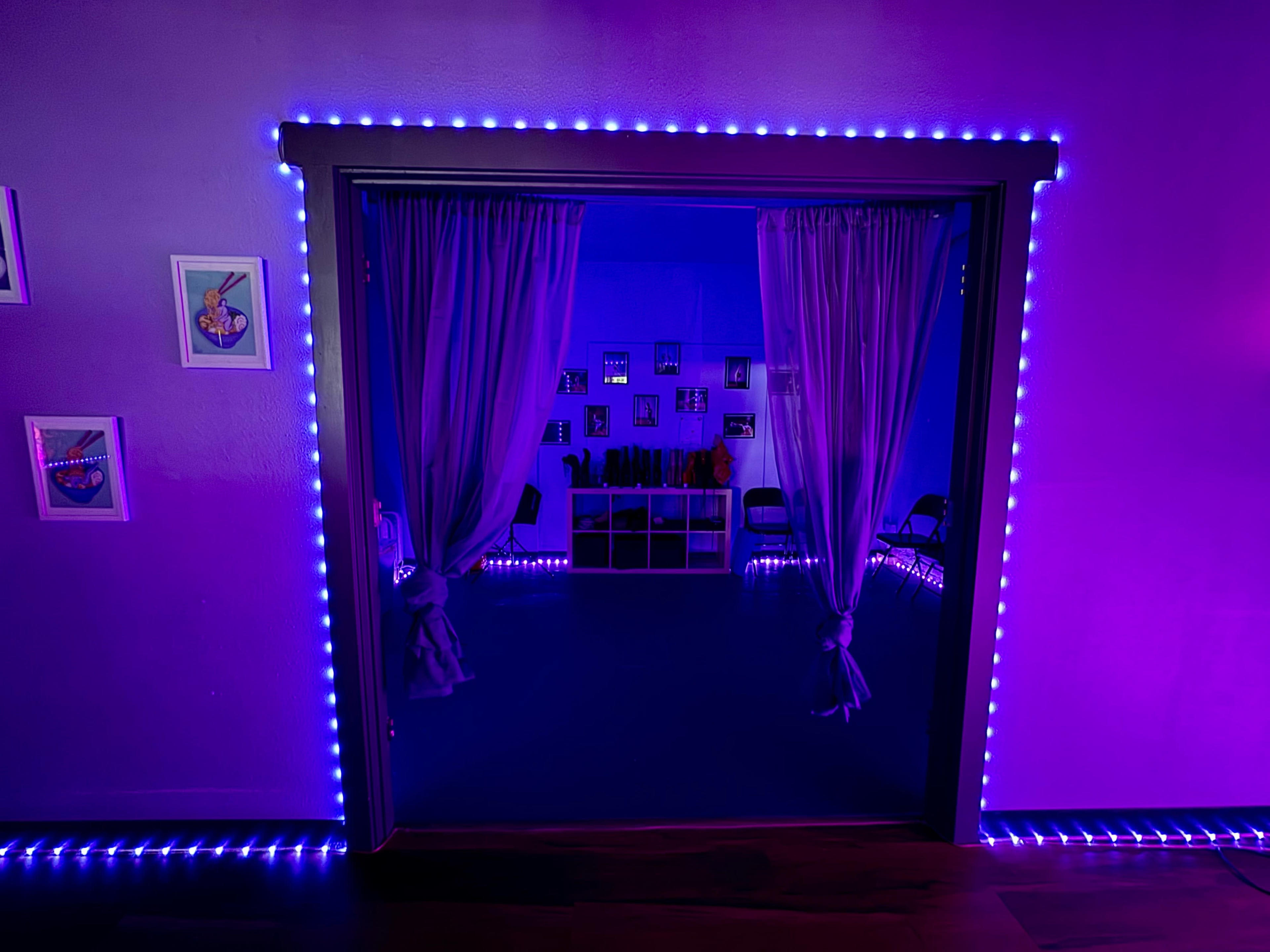 A doorway framed with purple LED lights leads into a room with chairs and framed artwork on the walls.