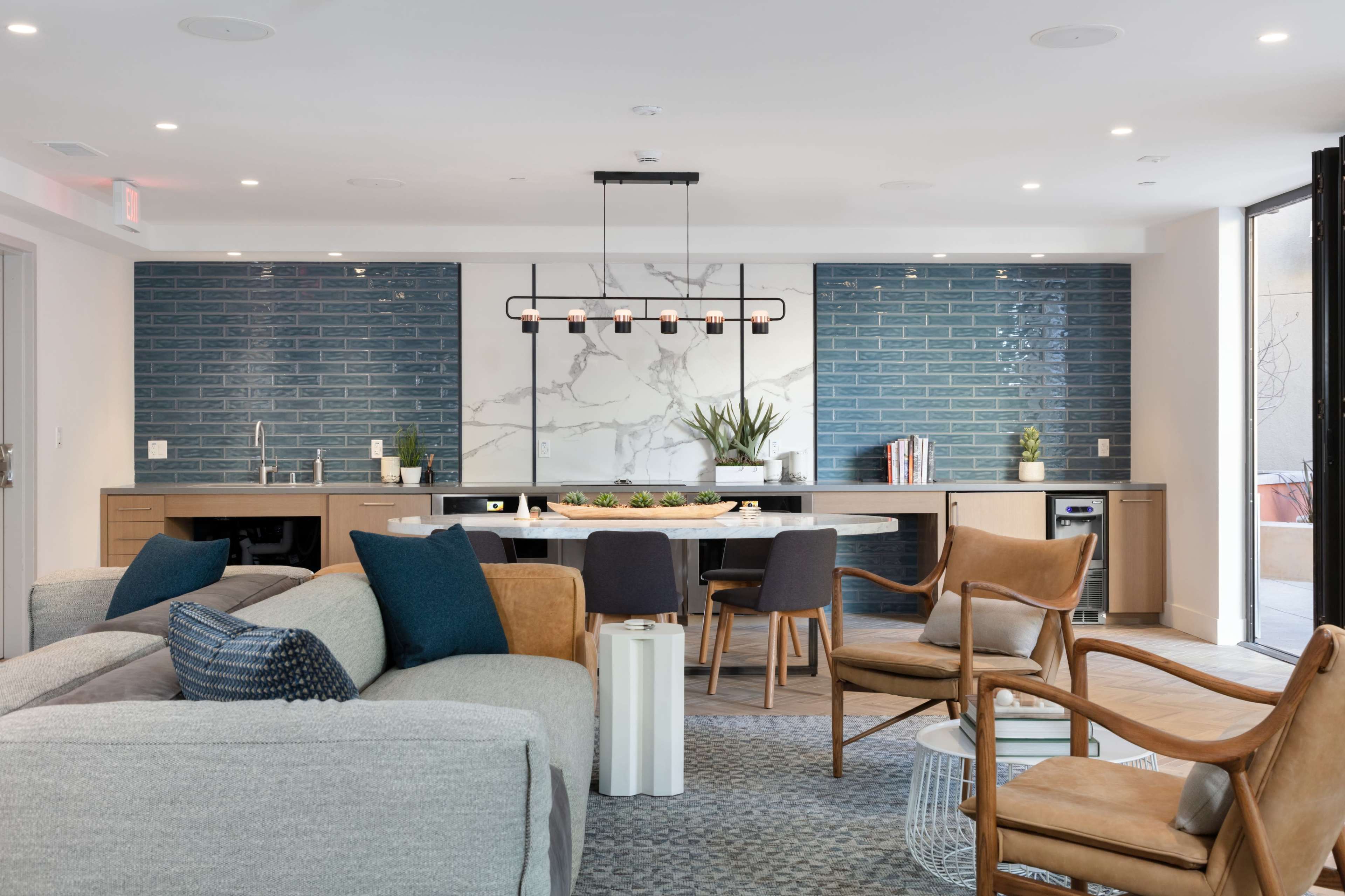 A modern lounge area with a kitchen featuring blue tile accents, a central dining table, and contemporary furniture arranged for comfort.
