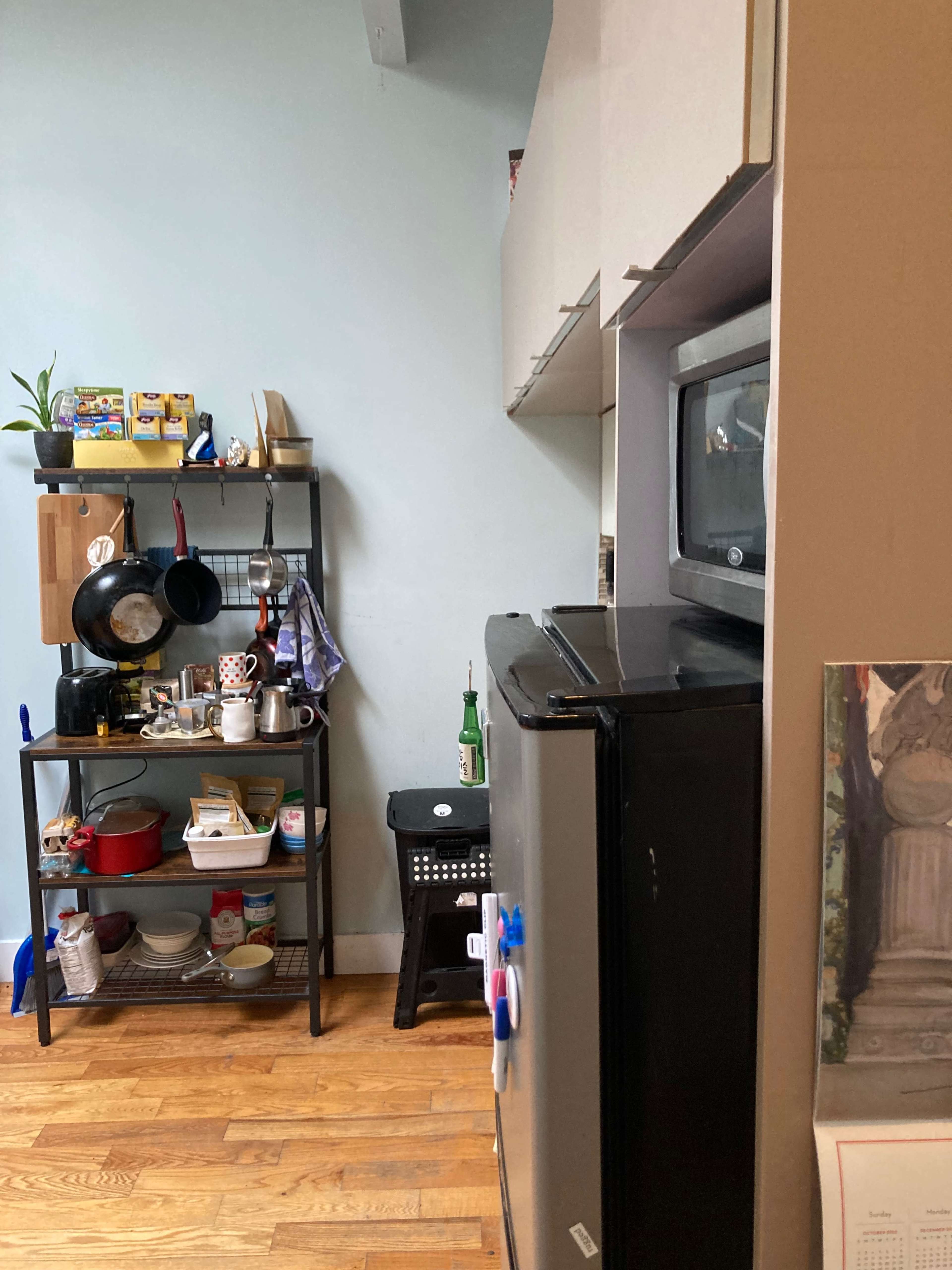 A kitchen area with cabinets, a black refrigerator, a microwave, and a storage cart with various kitchen items.