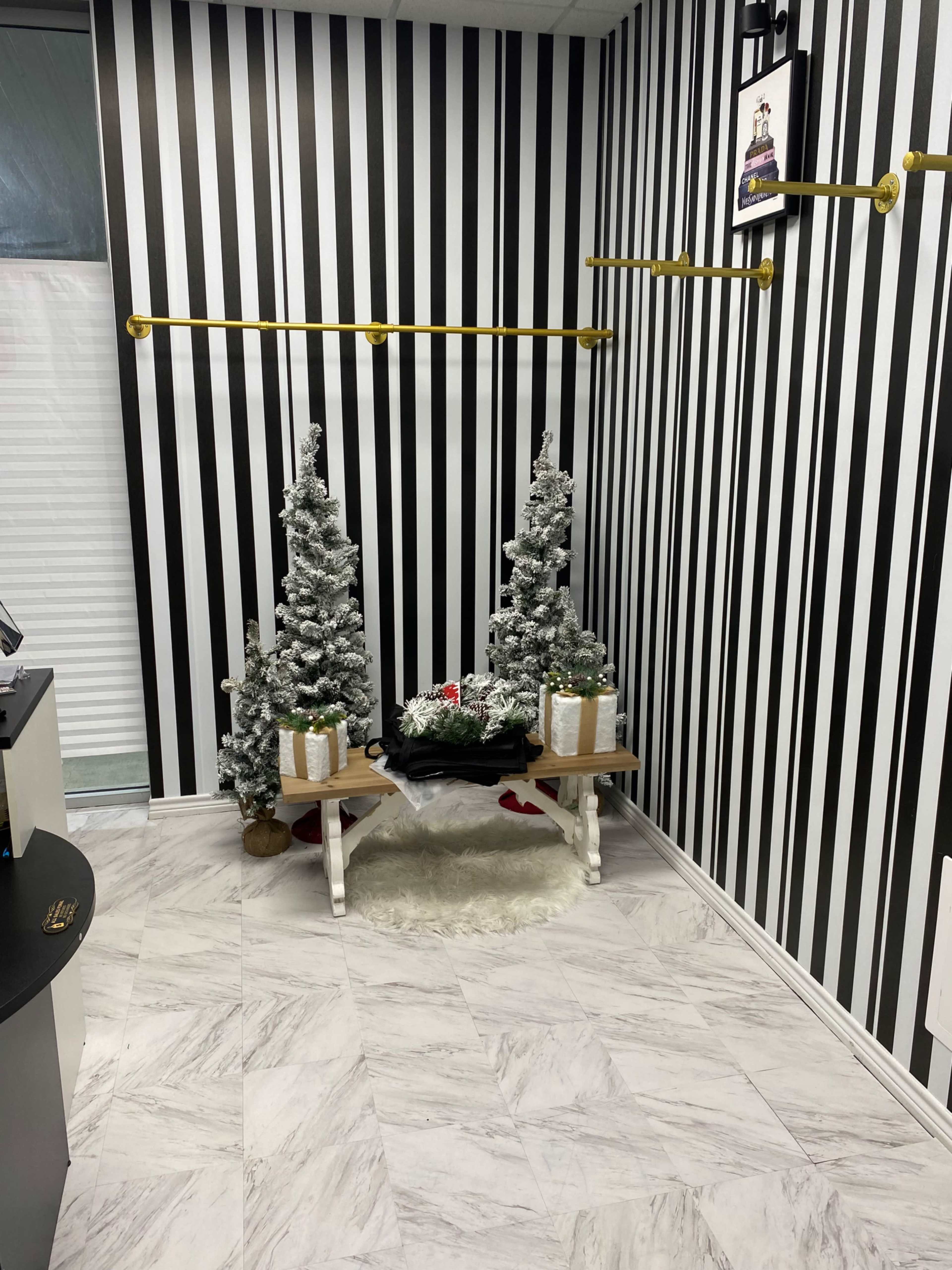 The scene shows a small indoor space with black and white striped walls, two artificial Christmas trees, and a decorated table with gifts.