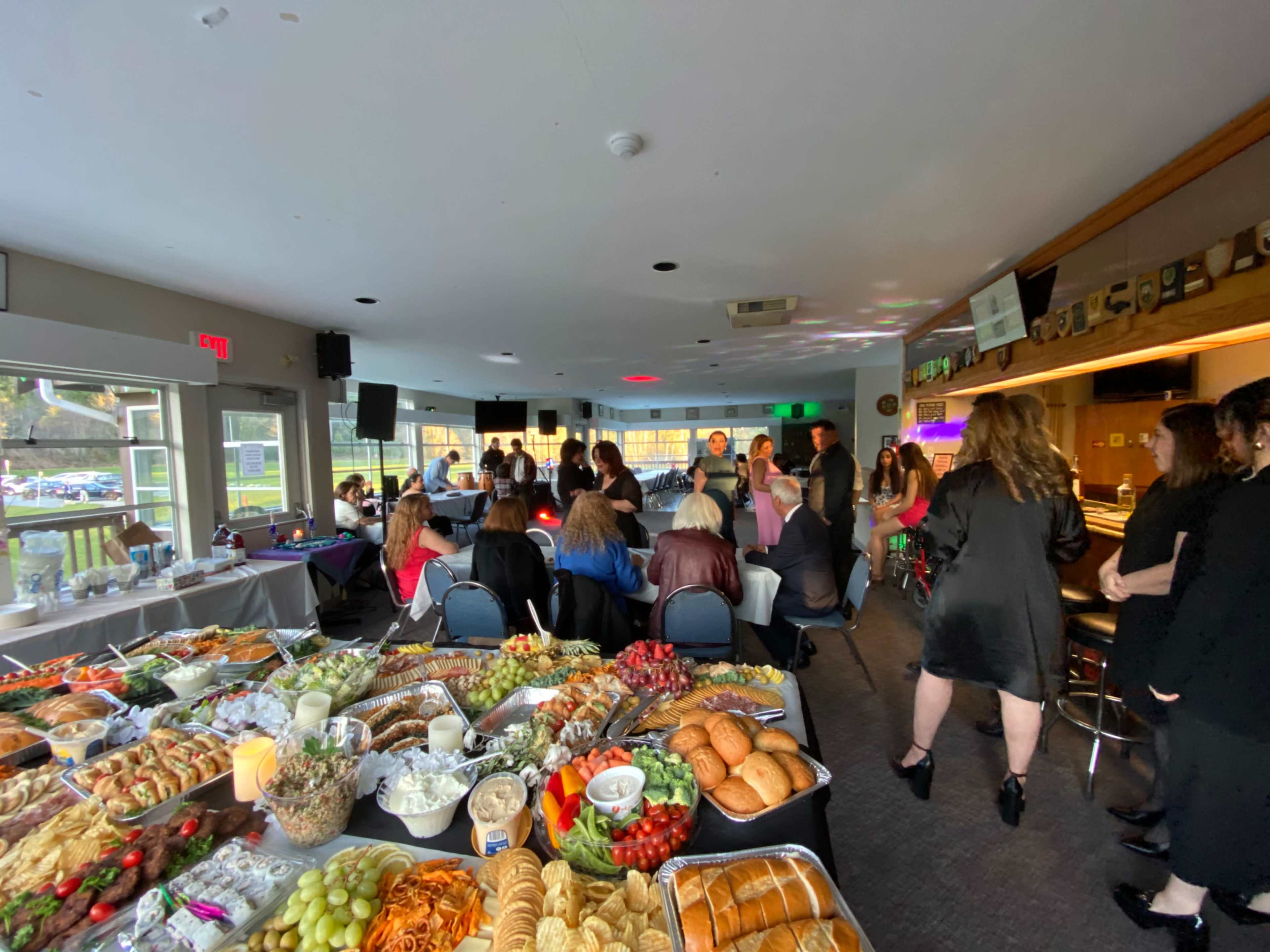 A banquet room filled with people mingling around tables laden with a variety of food and drinks.