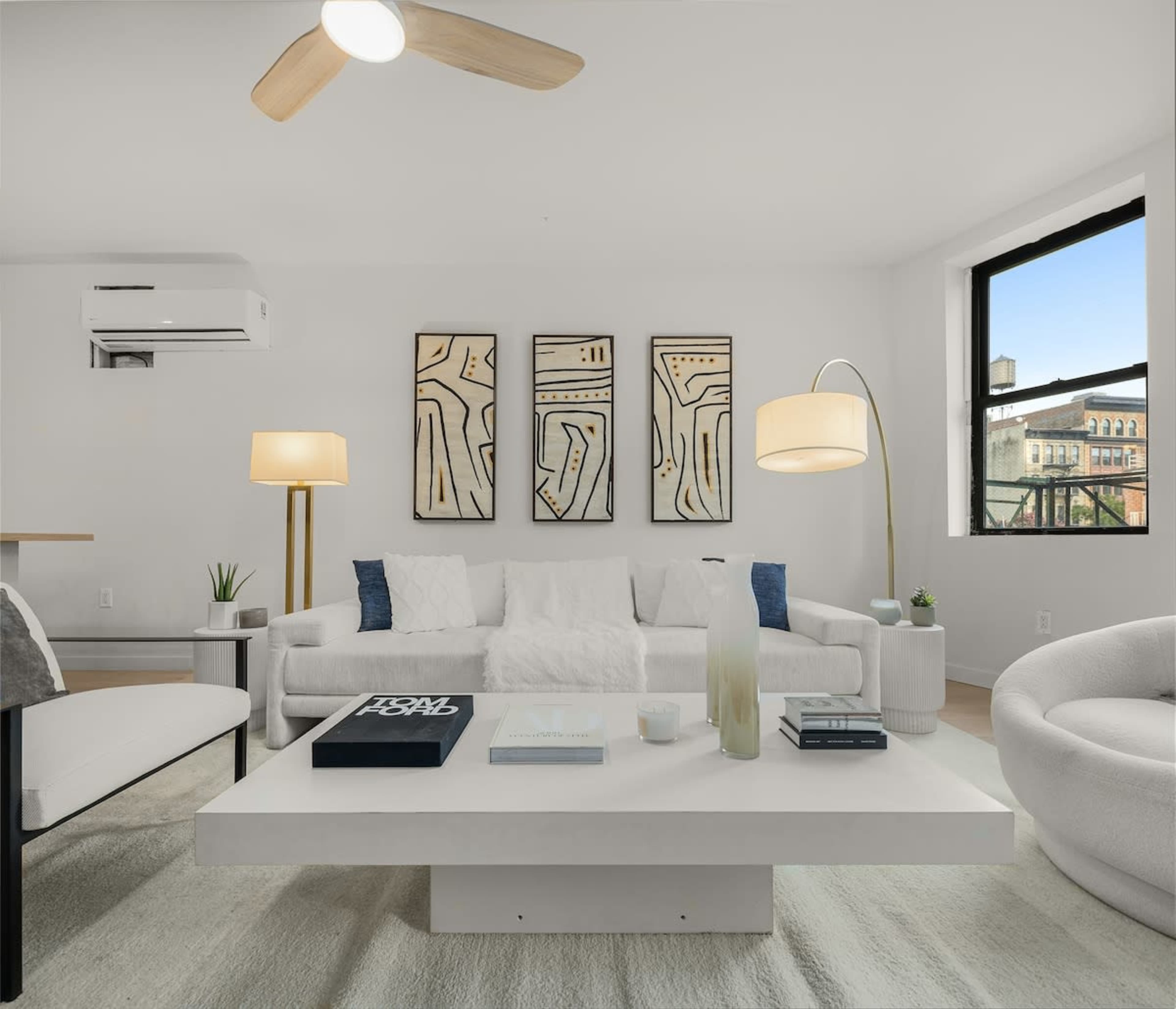 A modern living room featuring a white sofa, a round coffee table, and decorative wall art, with large windows allowing natural light to enter.